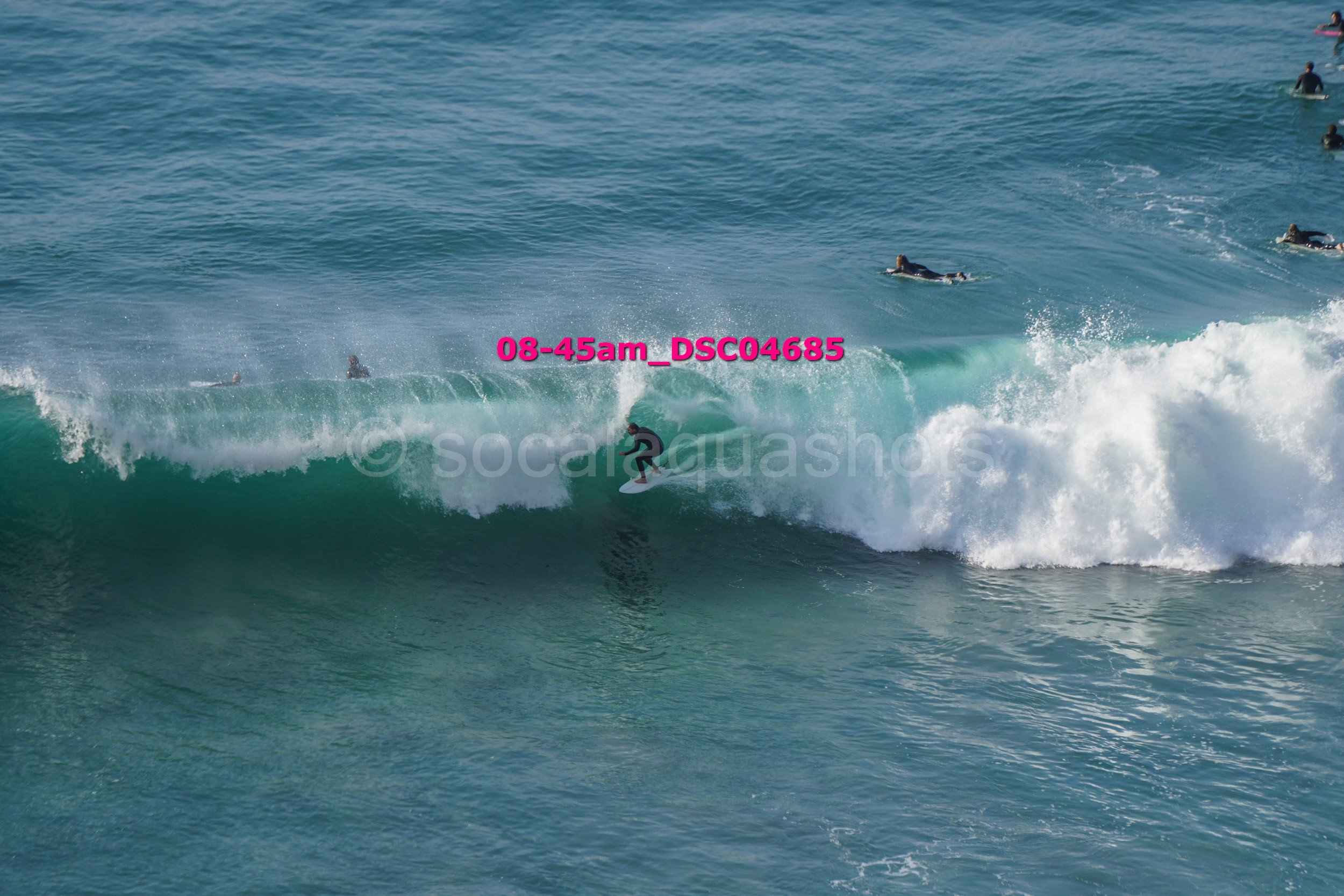 Surfer riding a wave at the beach, with several other surfers in the water nearby.
