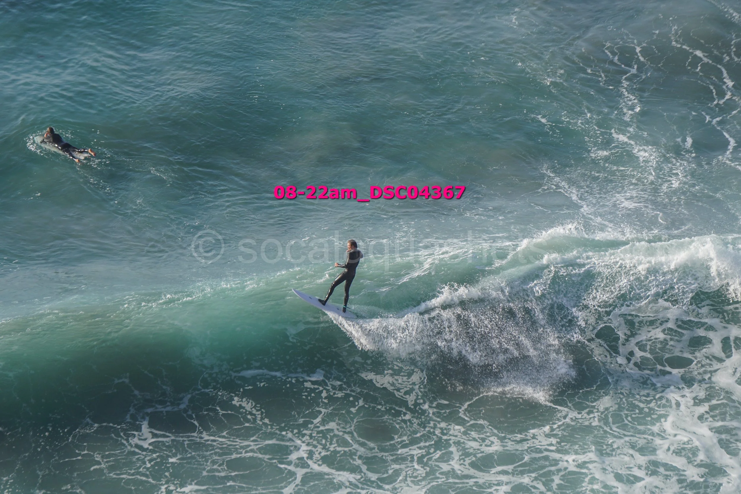 A person surfing on a wave in the ocean, with another person paddling in the background.