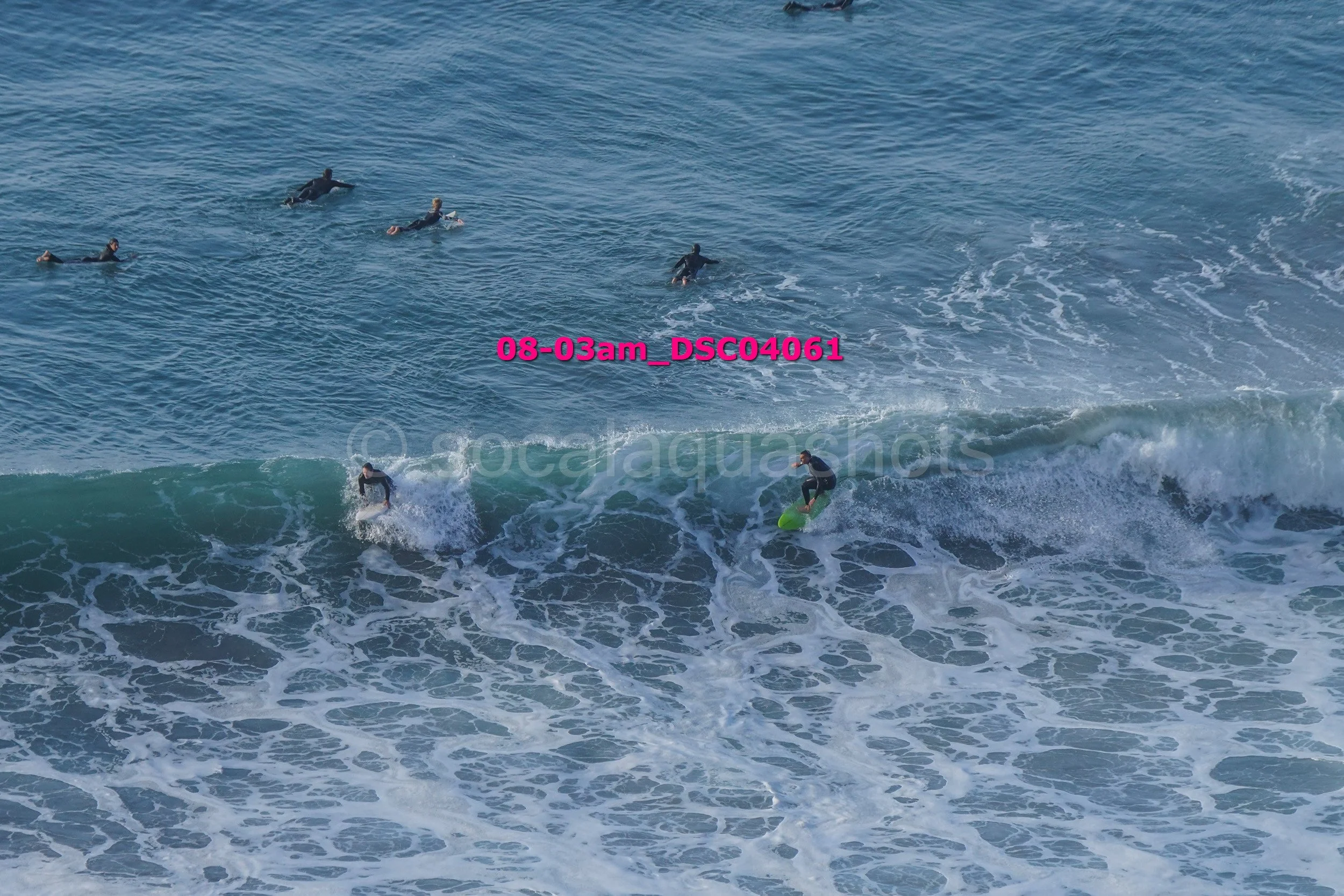 Surfers riding a wave in the ocean with others waiting in the water.