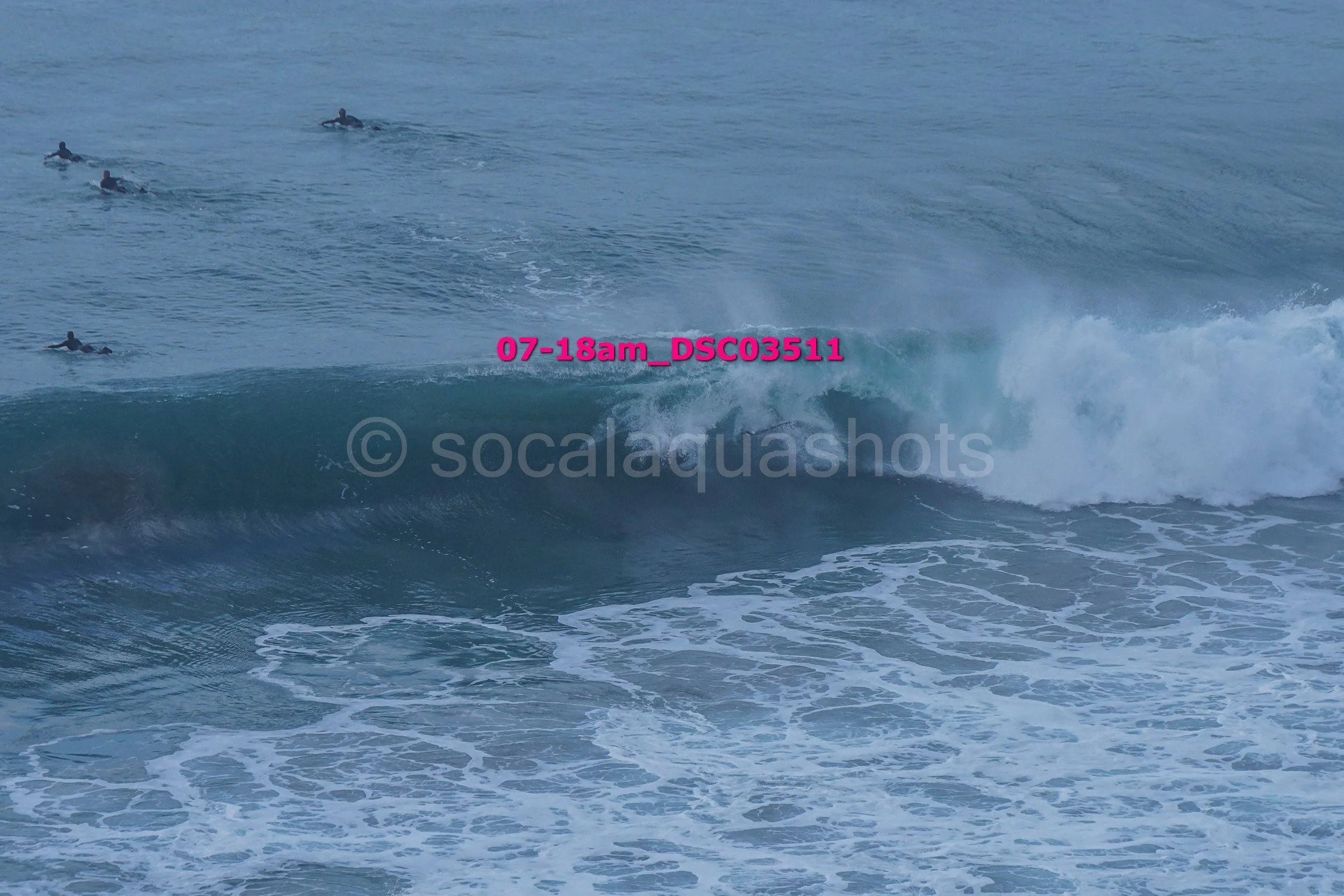A group of surfers riding and waiting for waves in the ocean with visible white foam and blue water.