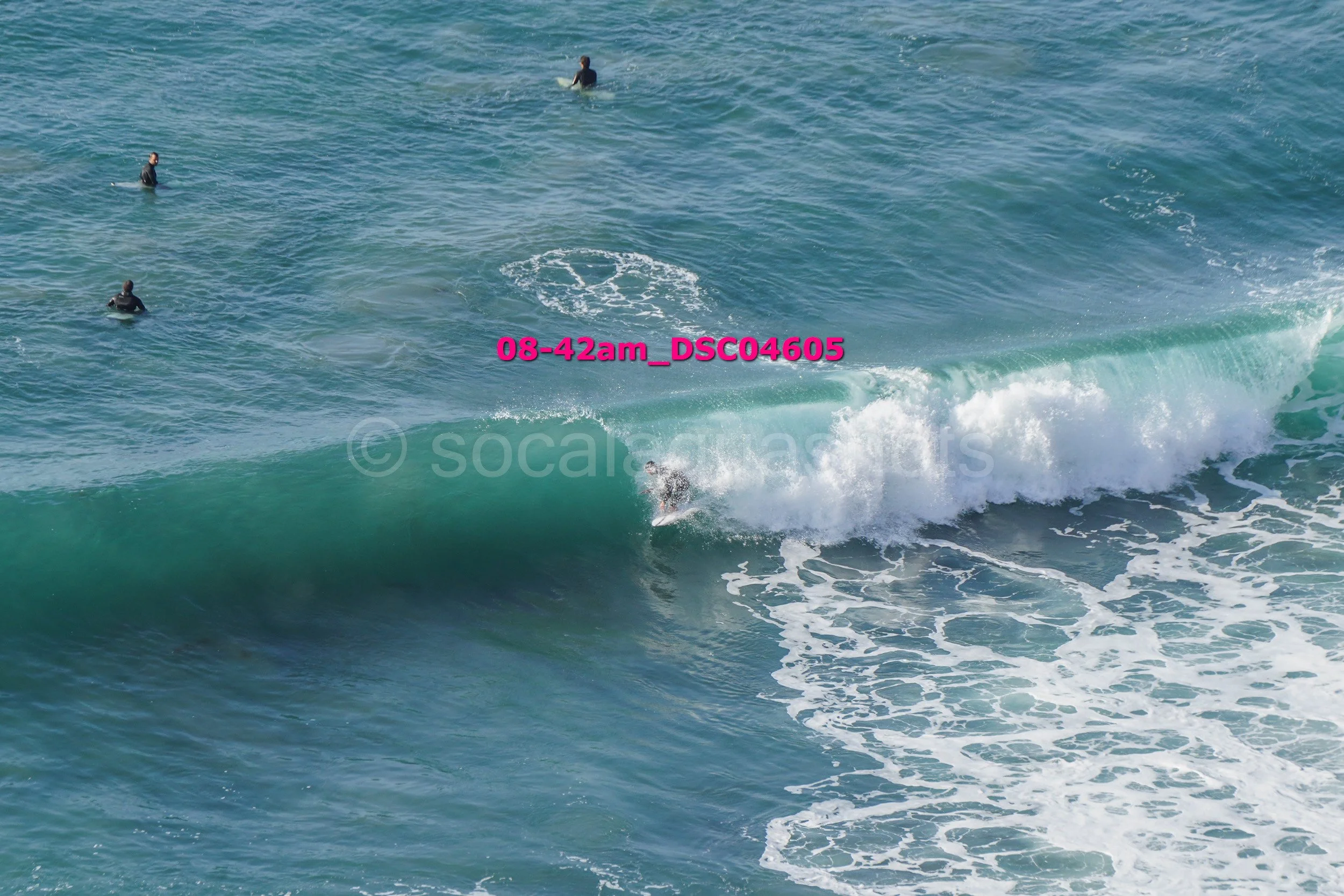 Surfer riding a wave with four surfers watching in the water.
