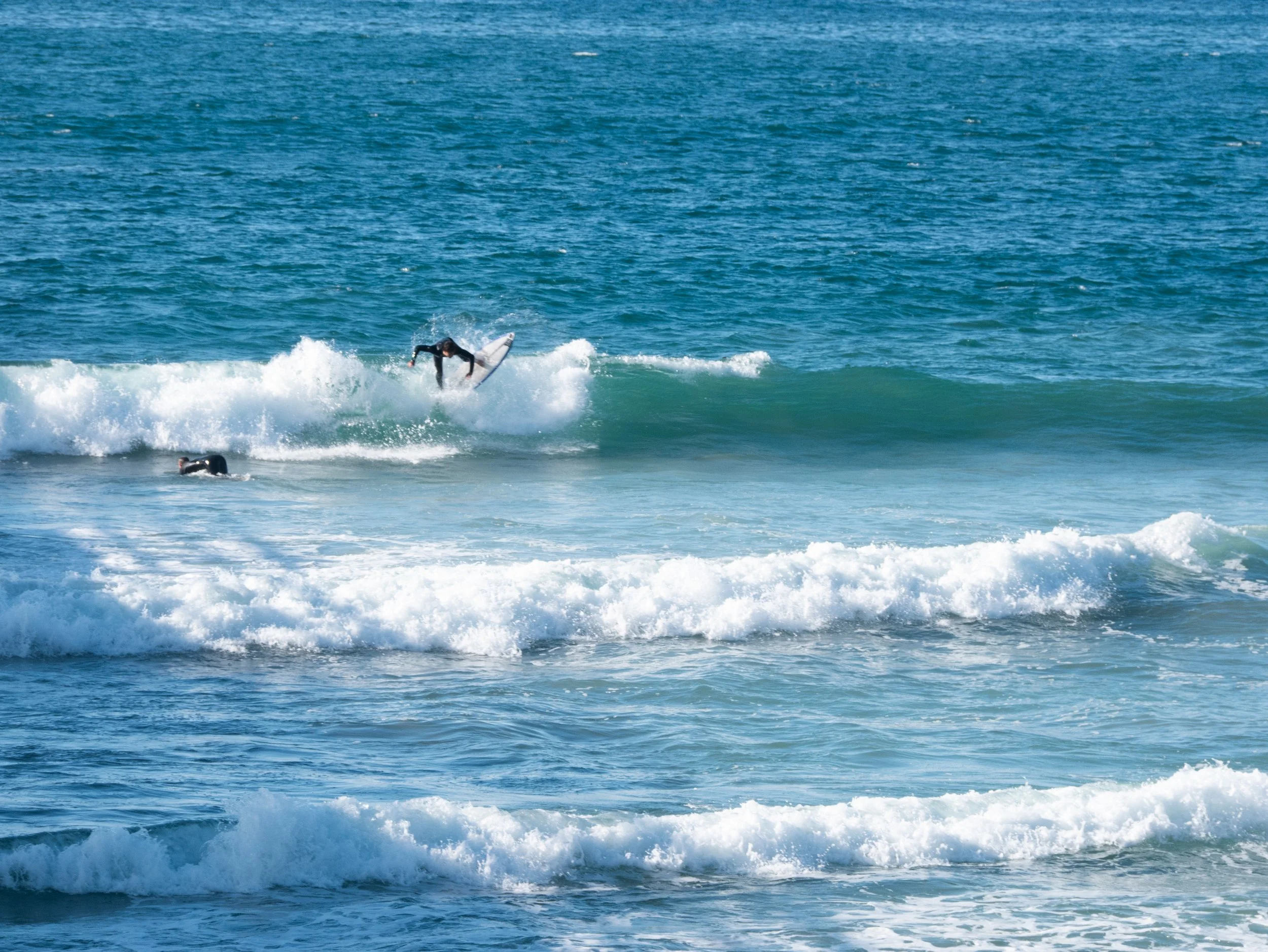 A person surfing on a wave in the ocean, with another swimmer or surfer nearby