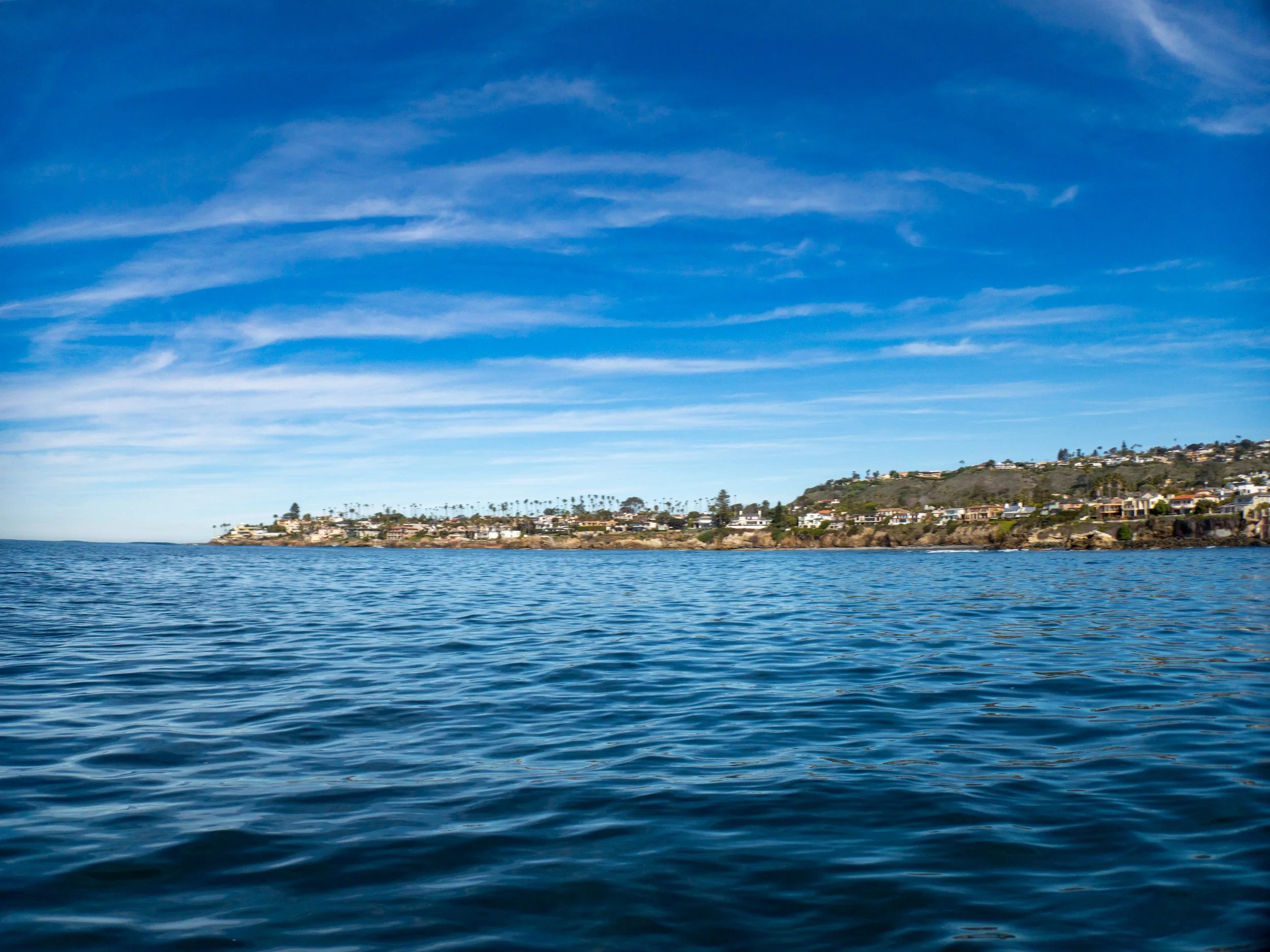 View of the ocean with houses along the shoreline and a clear, blue sky above.