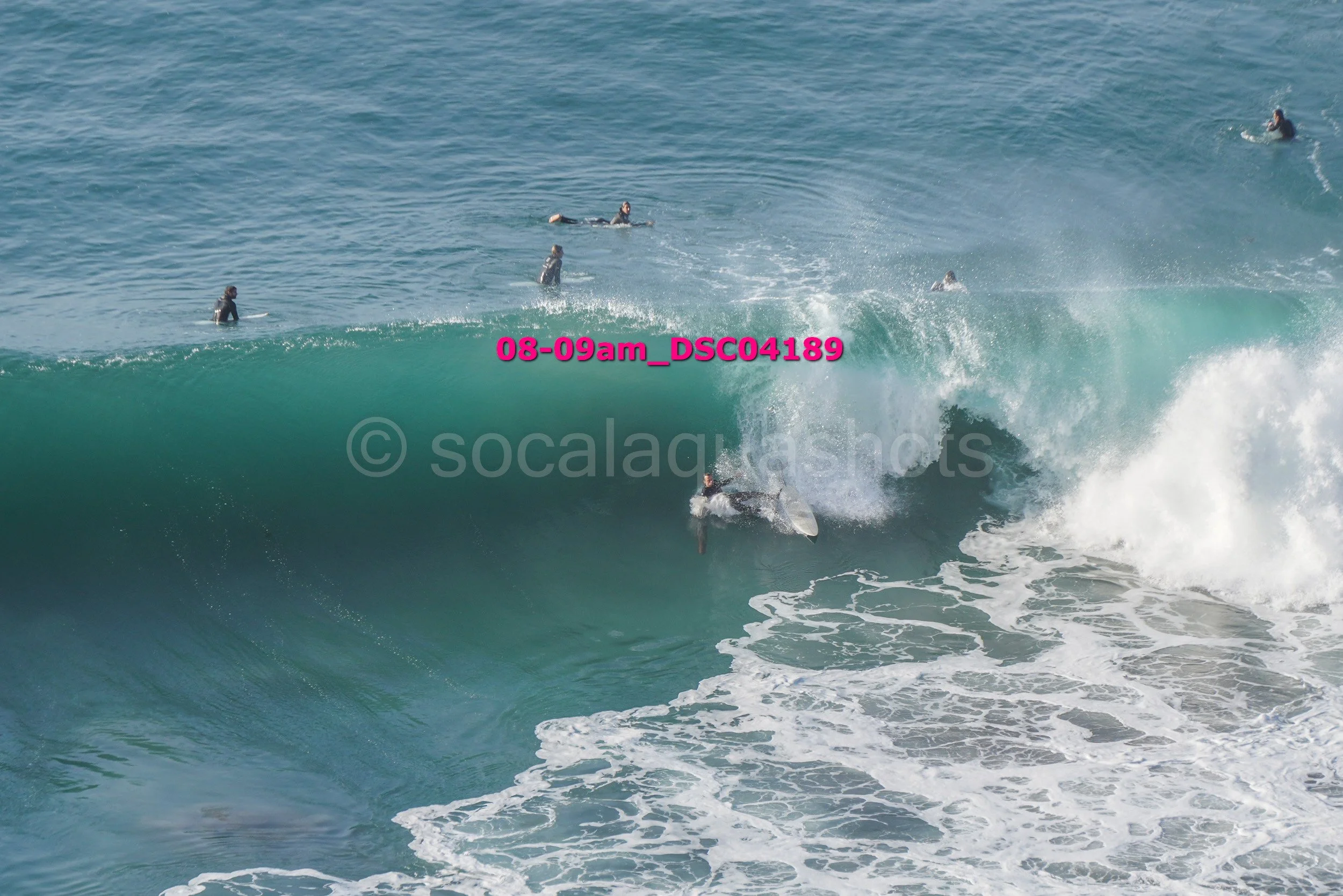 Surfer riding a large wave while other surfers wait and watch in the water.