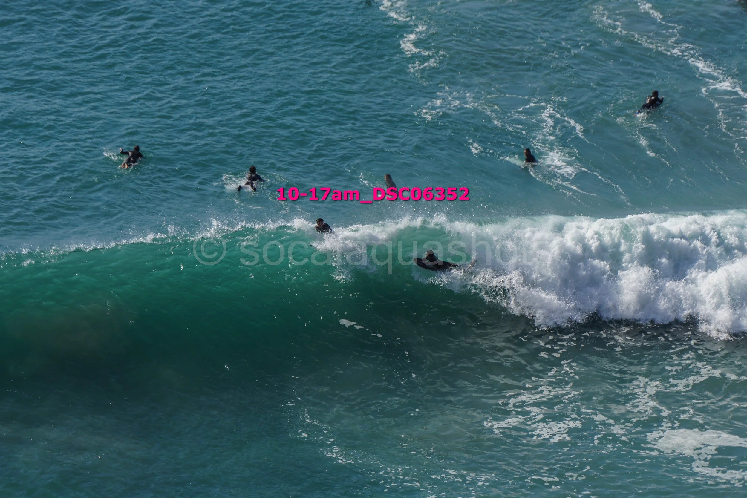 Surfers in wetsuits riding and swimming in the ocean waves.