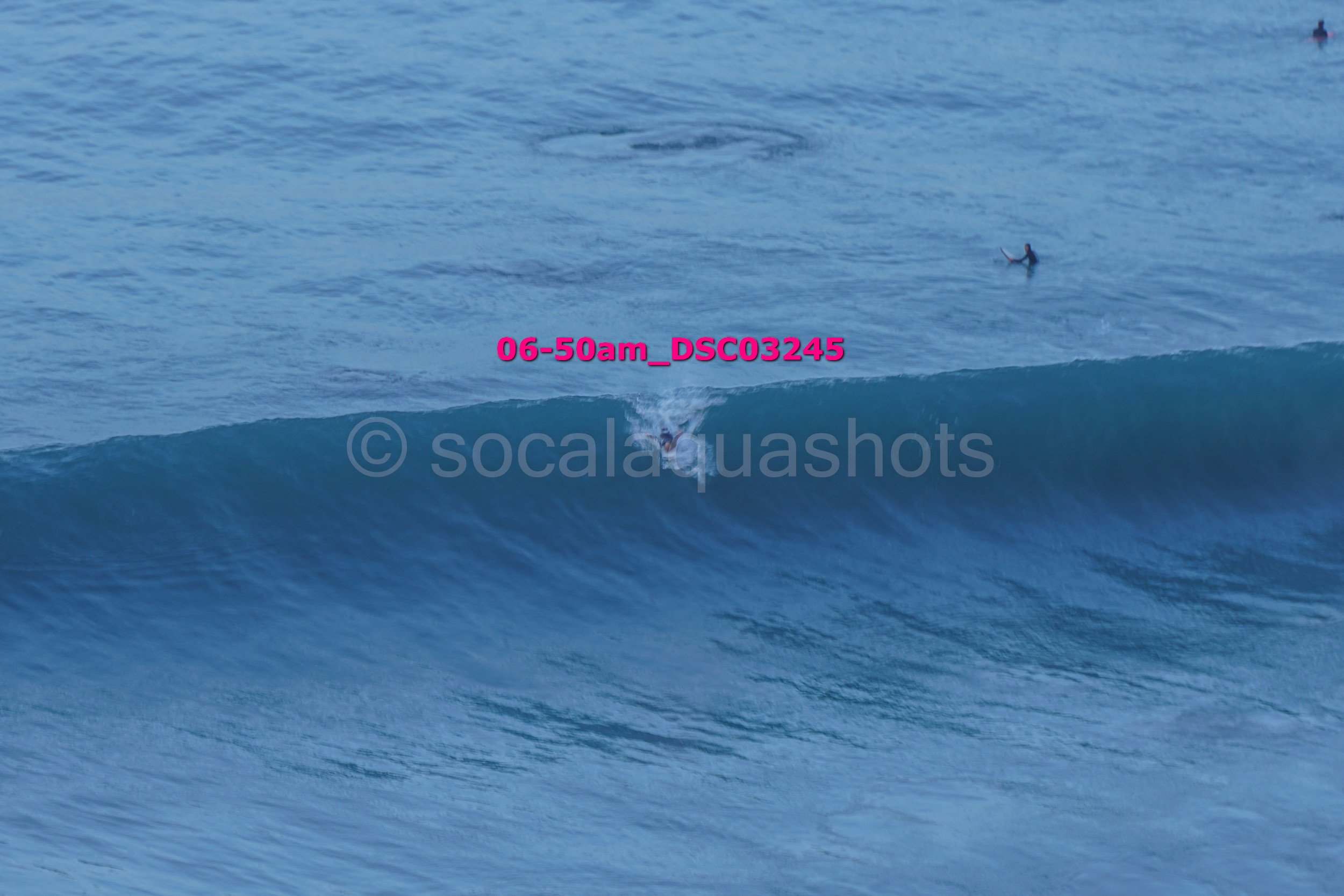 Surfer riding a large wave in the ocean during early morning with other surfers visible in the water.