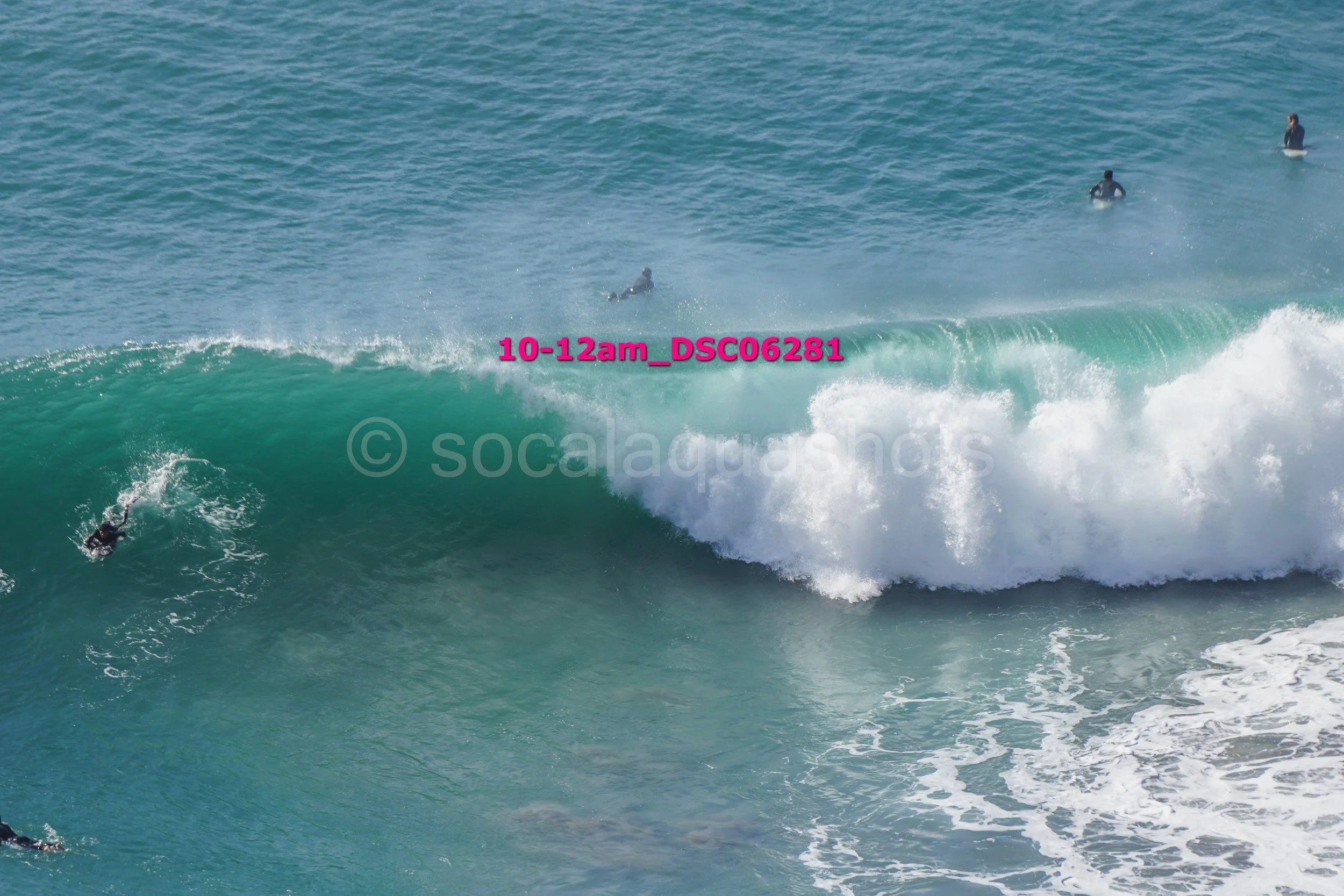 Surfers riding large ocean waves with one surfer falling off the wave and others waiting on surfboards in the background