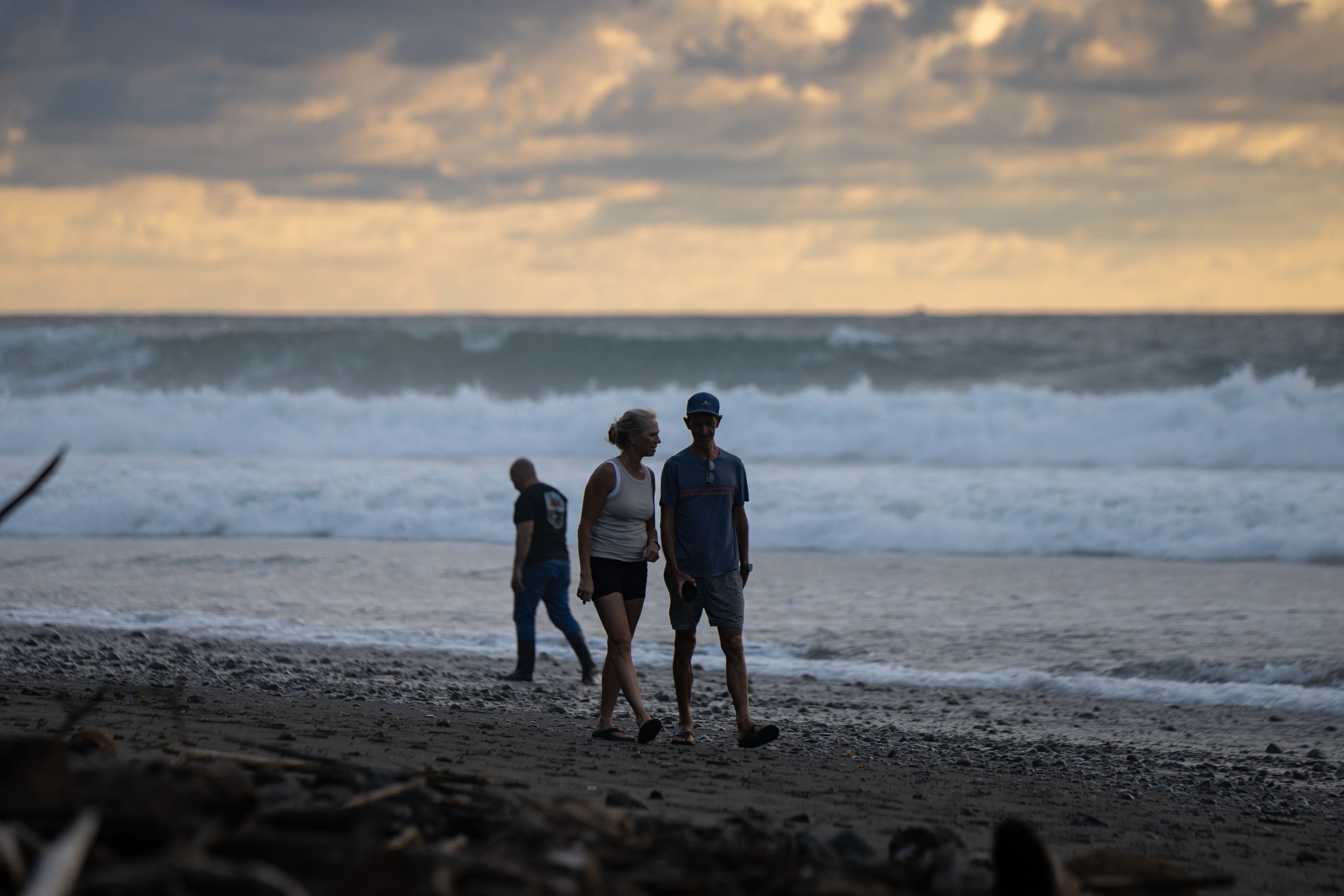 People walking along the beach at sunset with ocean waves in the background.
