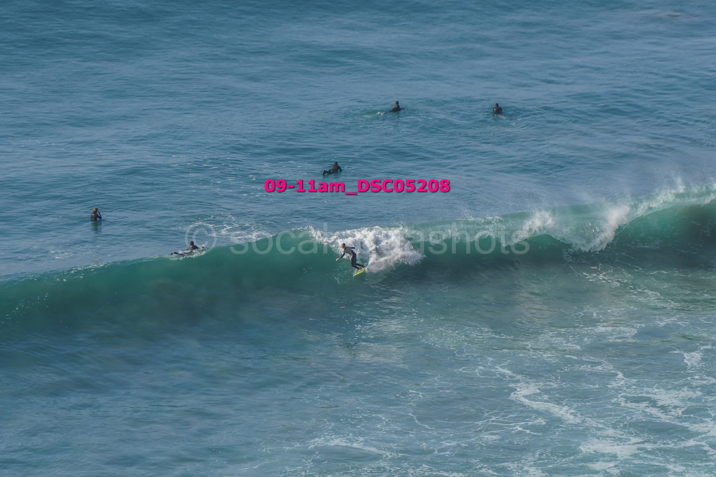 A person surfing on a wave in the ocean with several other people in the water nearby.