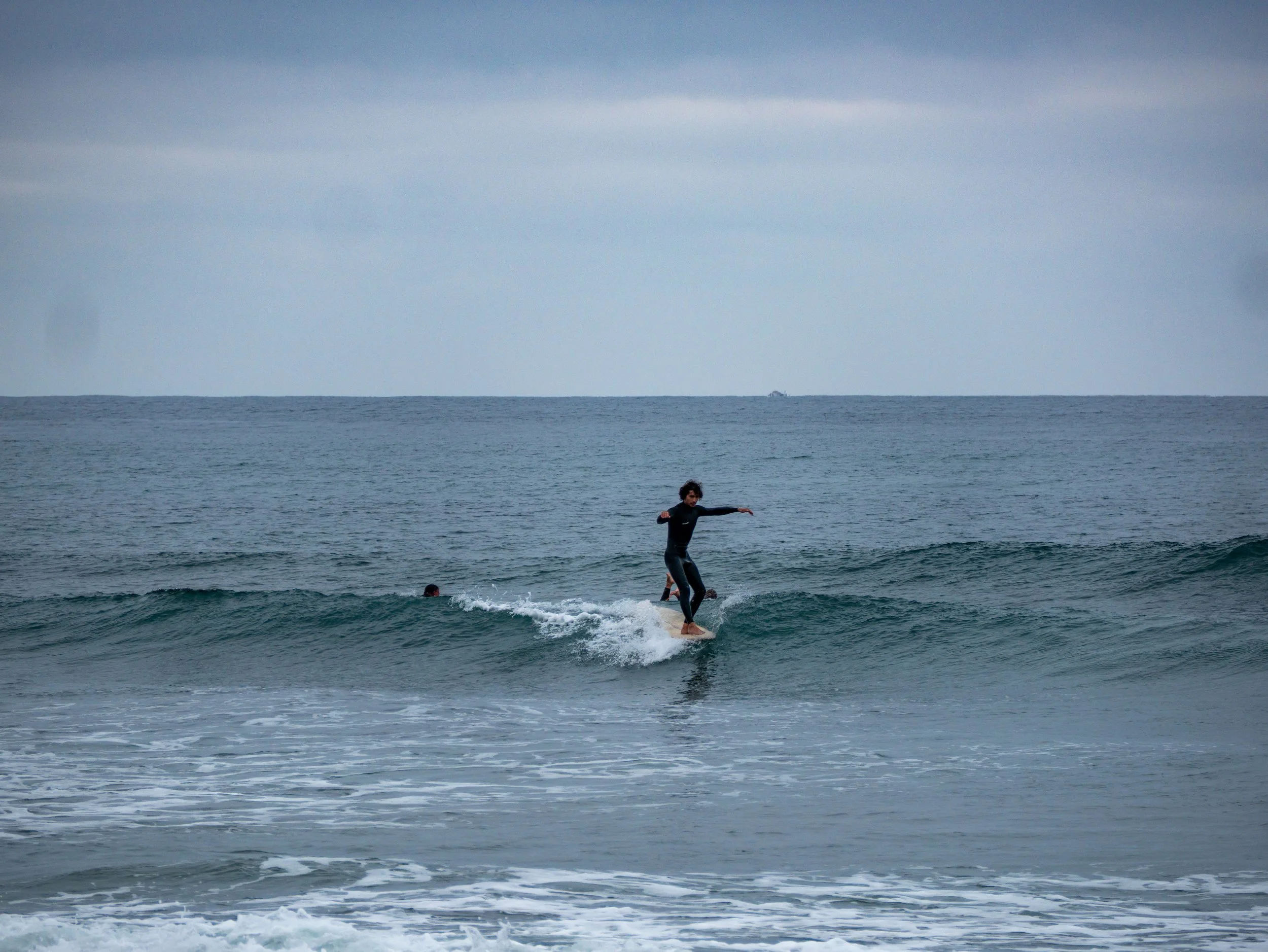 A person surfing on a small wave in the ocean, with dark clouds overhead.