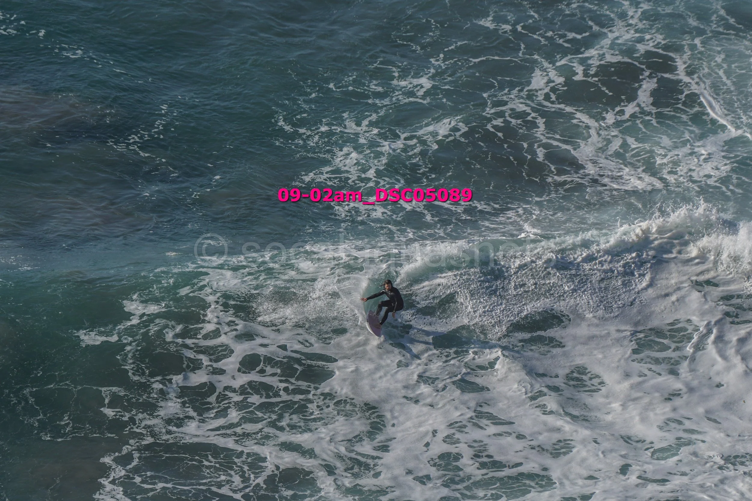 A person surfing on a wave in the ocean, wearing a dark wetsuit.