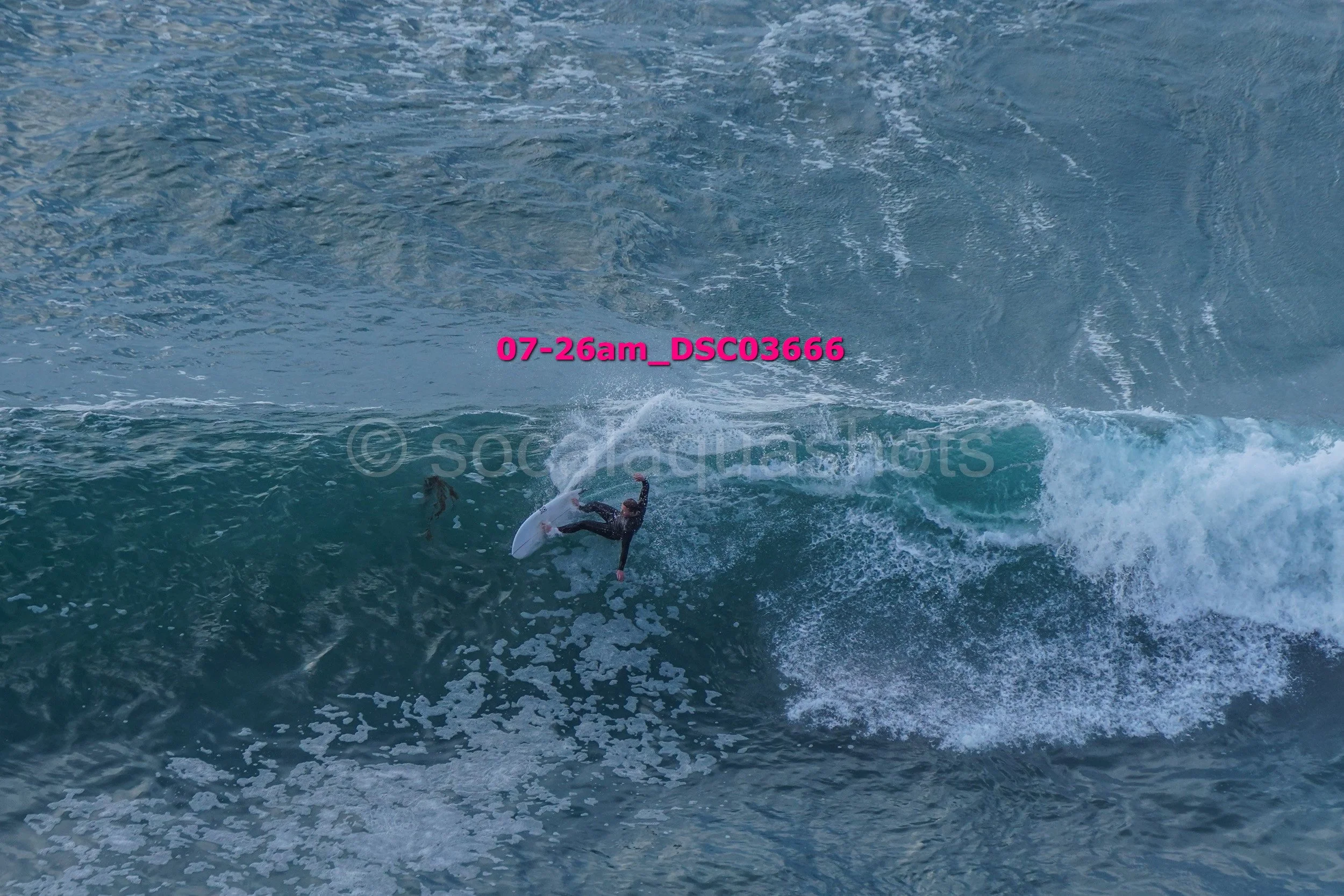 A person surfing on a wave in the ocean, wearing a wetsuit and holding a surfboard, with water splashing around.