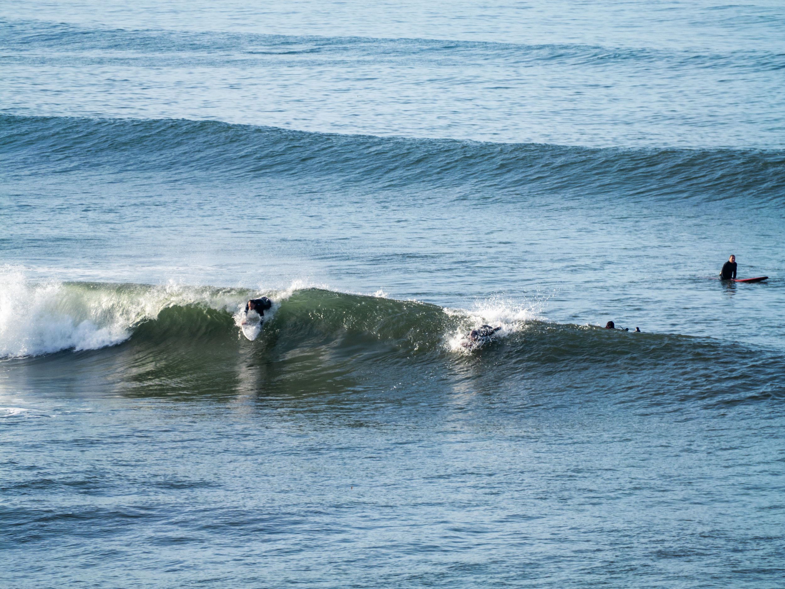 Two surfers riding a wave in the ocean with other surfers in the water and a person on a paddleboard in the background.