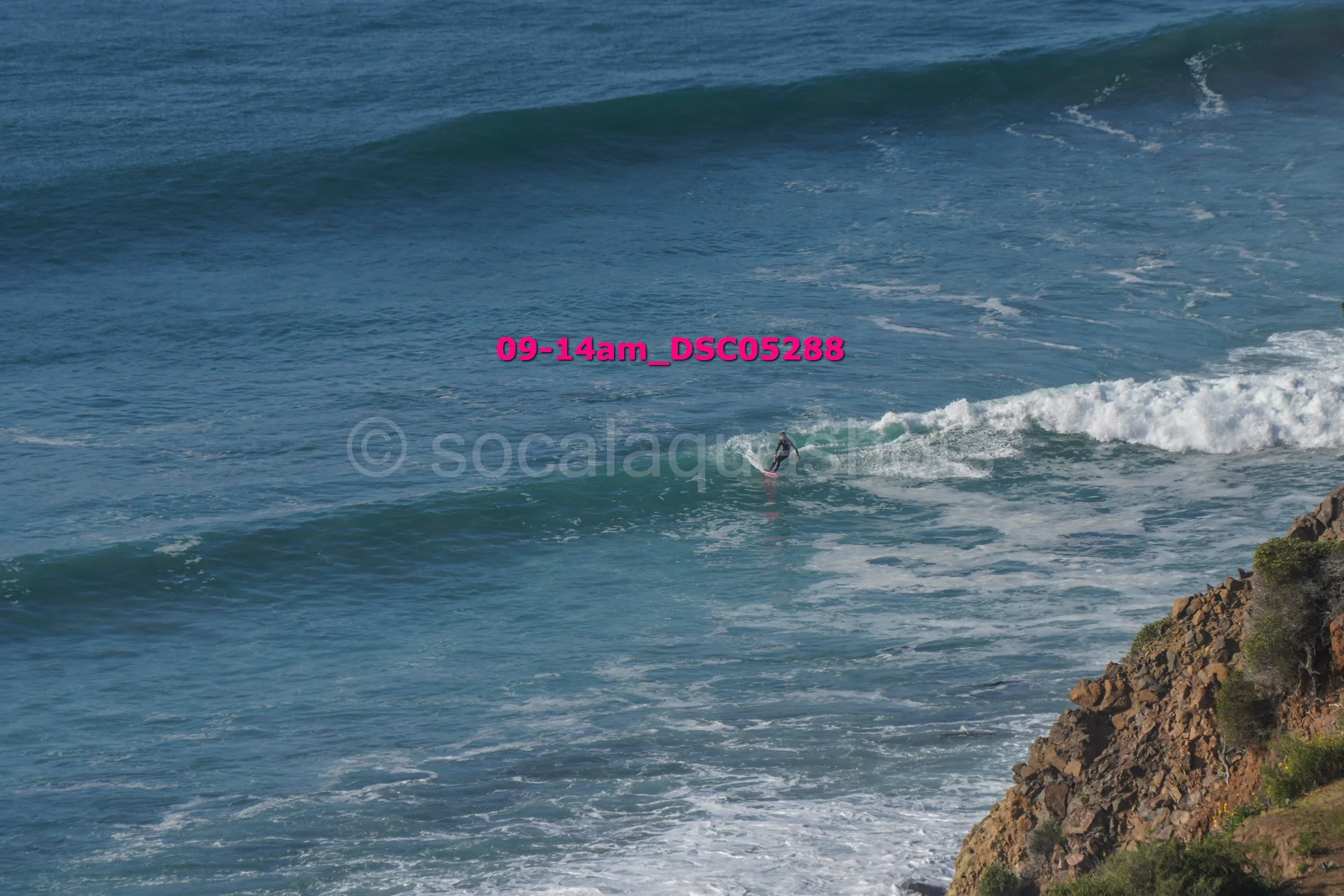 A person surfing on a wave near a rocky coastline in the ocean.