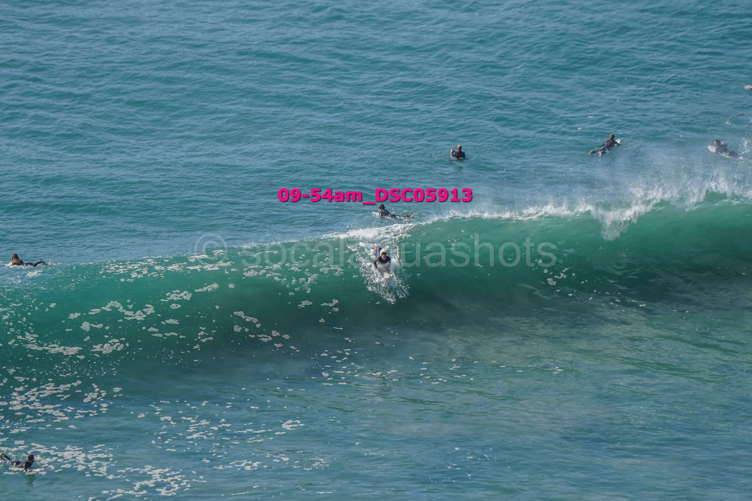 People surfing and swimming in ocean waves on a sunny day.