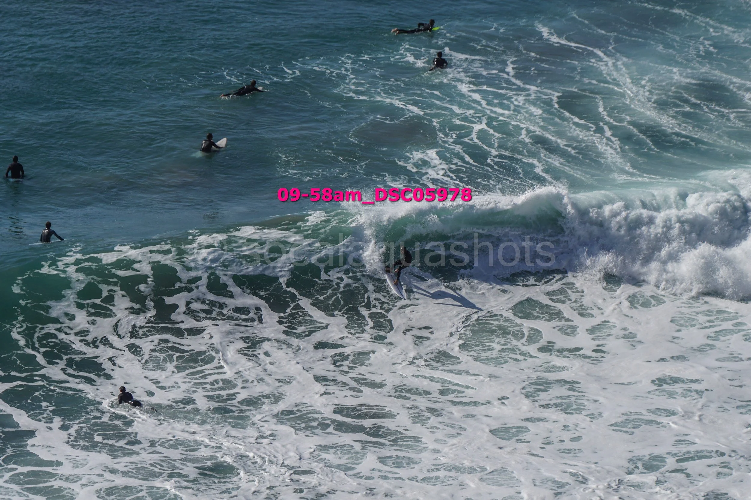 Surfer riding a wave at the beach with multiple people in the water