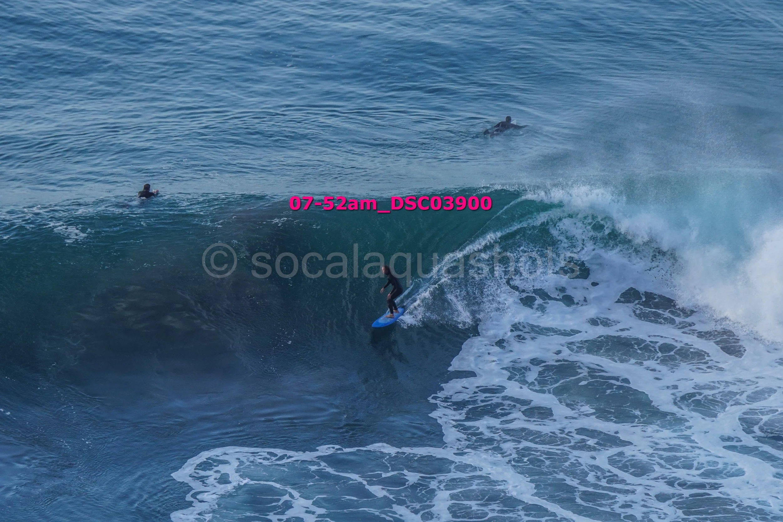 Surfer riding a large wave while two other surfers are seen swimming in the ocean.