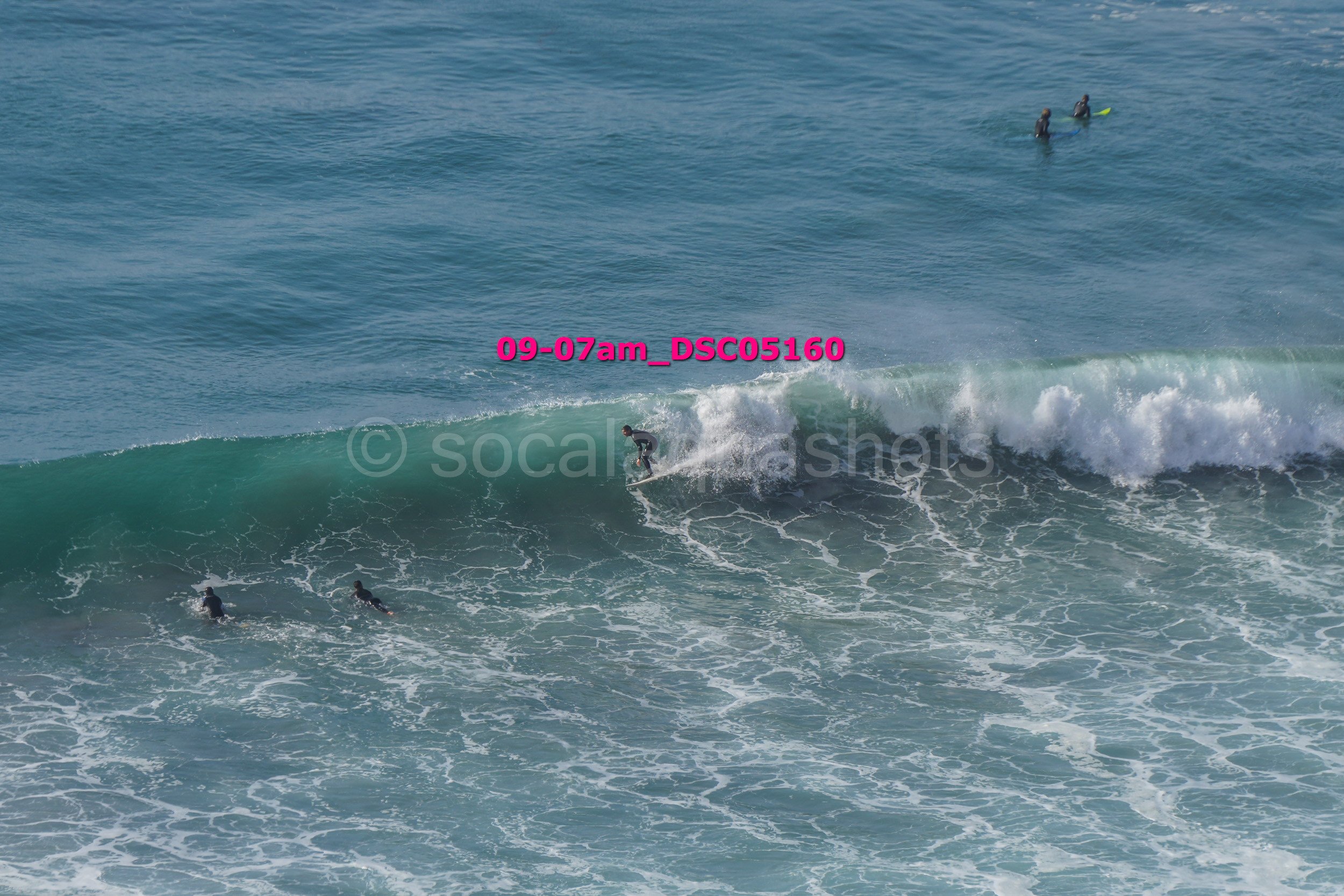 People surfing in the ocean, with some waiting in the water and one person riding a wave.