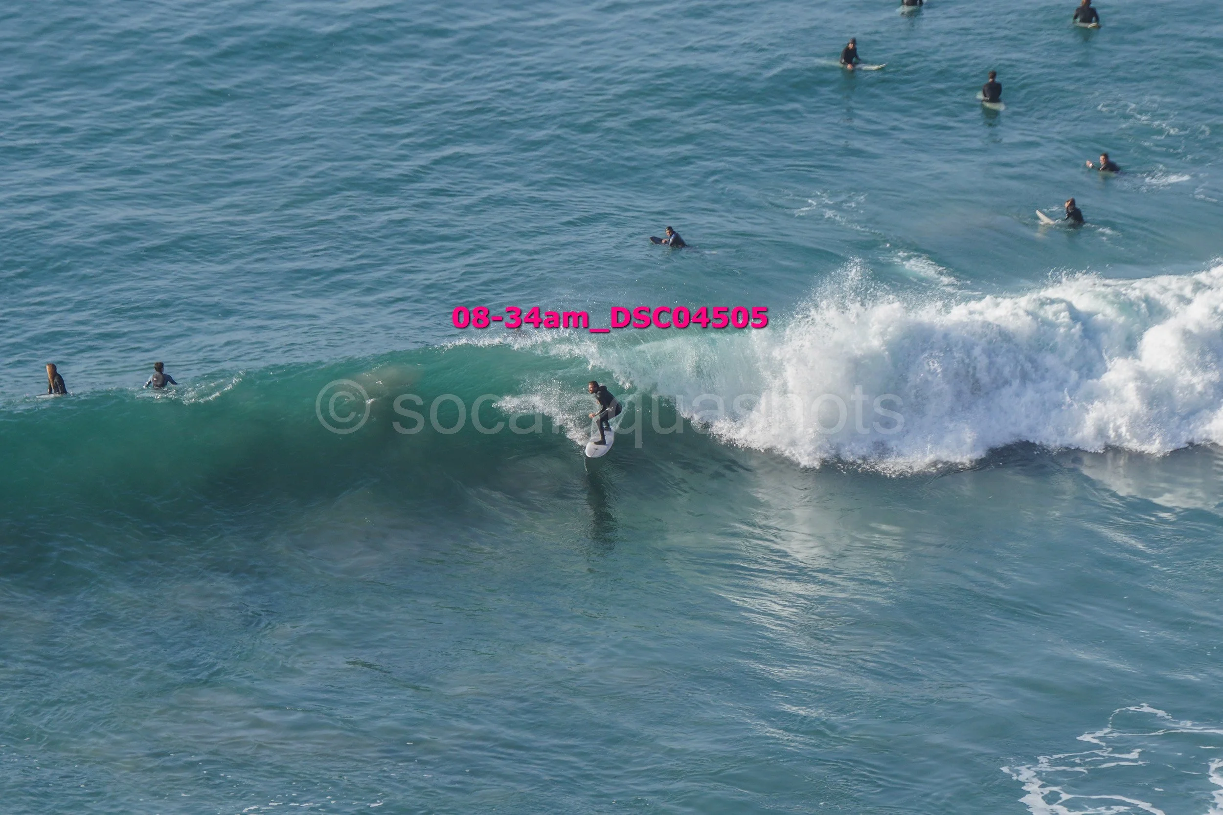 Surfer riding a wave while multiple surfers watch from the water.
