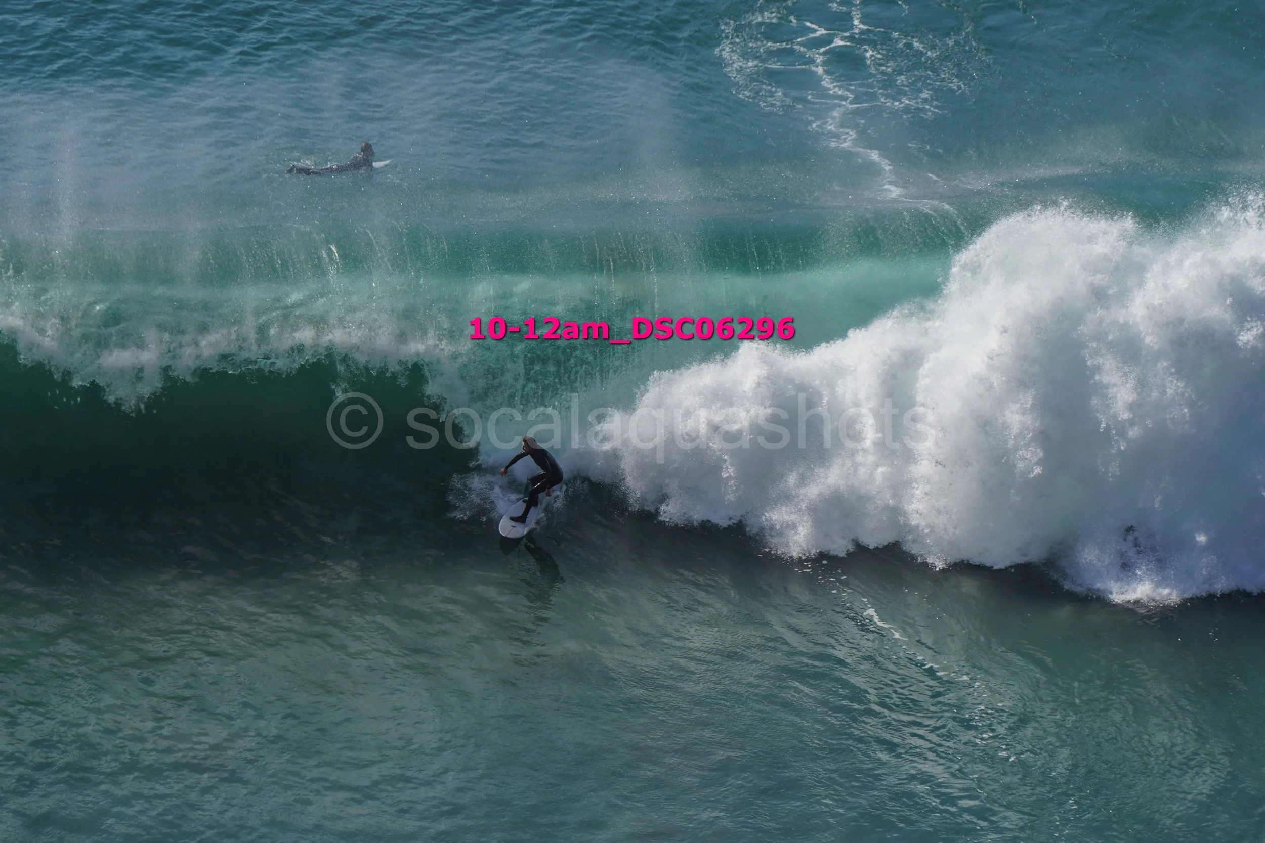A person surfing on a wave in the ocean, with another surfer visible in the distance.