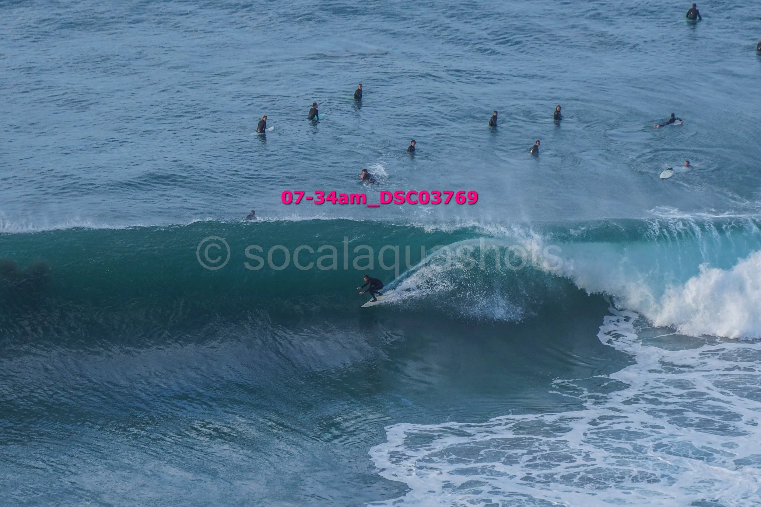 Surfer riding a wave with several people swimming in the ocean in the background.