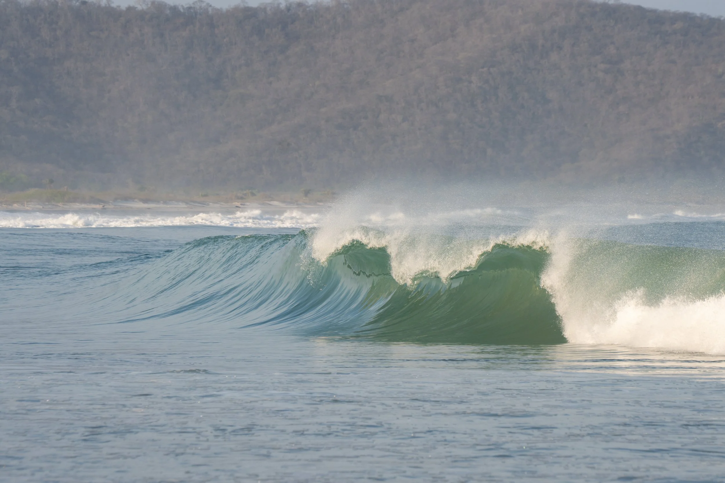 Ocean waves crashing near the shore with a mountain range in the background.