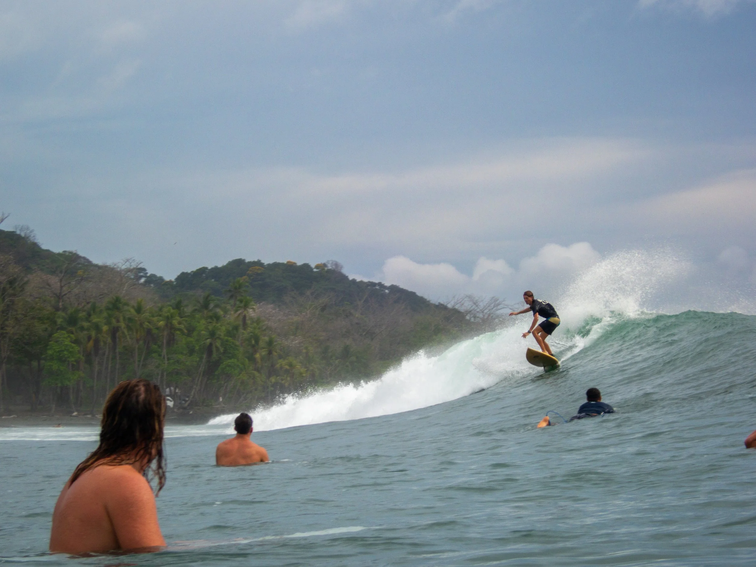 Surfer riding a wave with observers in water, tropical background