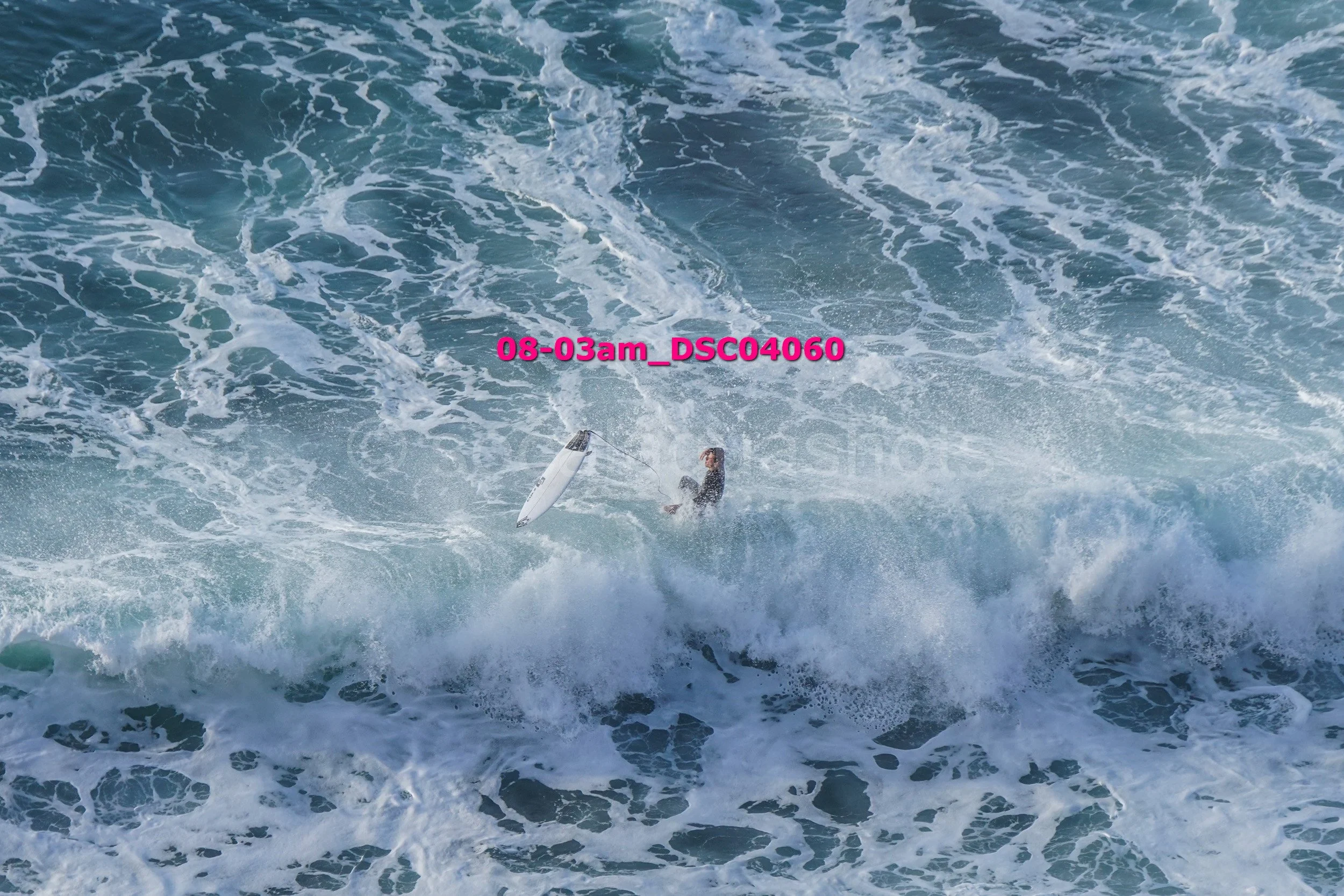 A person in the ocean holding a surfboard amidst large waves.