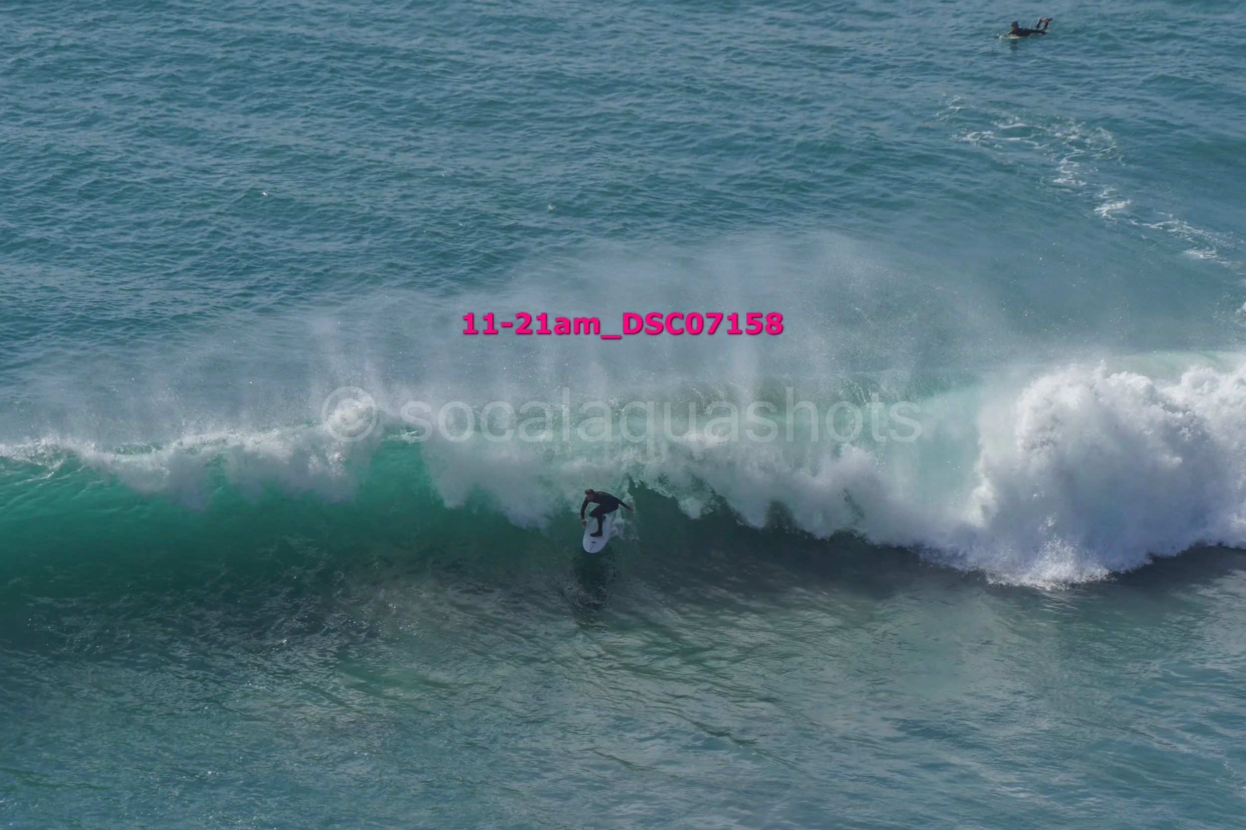 A person surfing on a wave in the ocean, with another person on a surfboard visible in the background