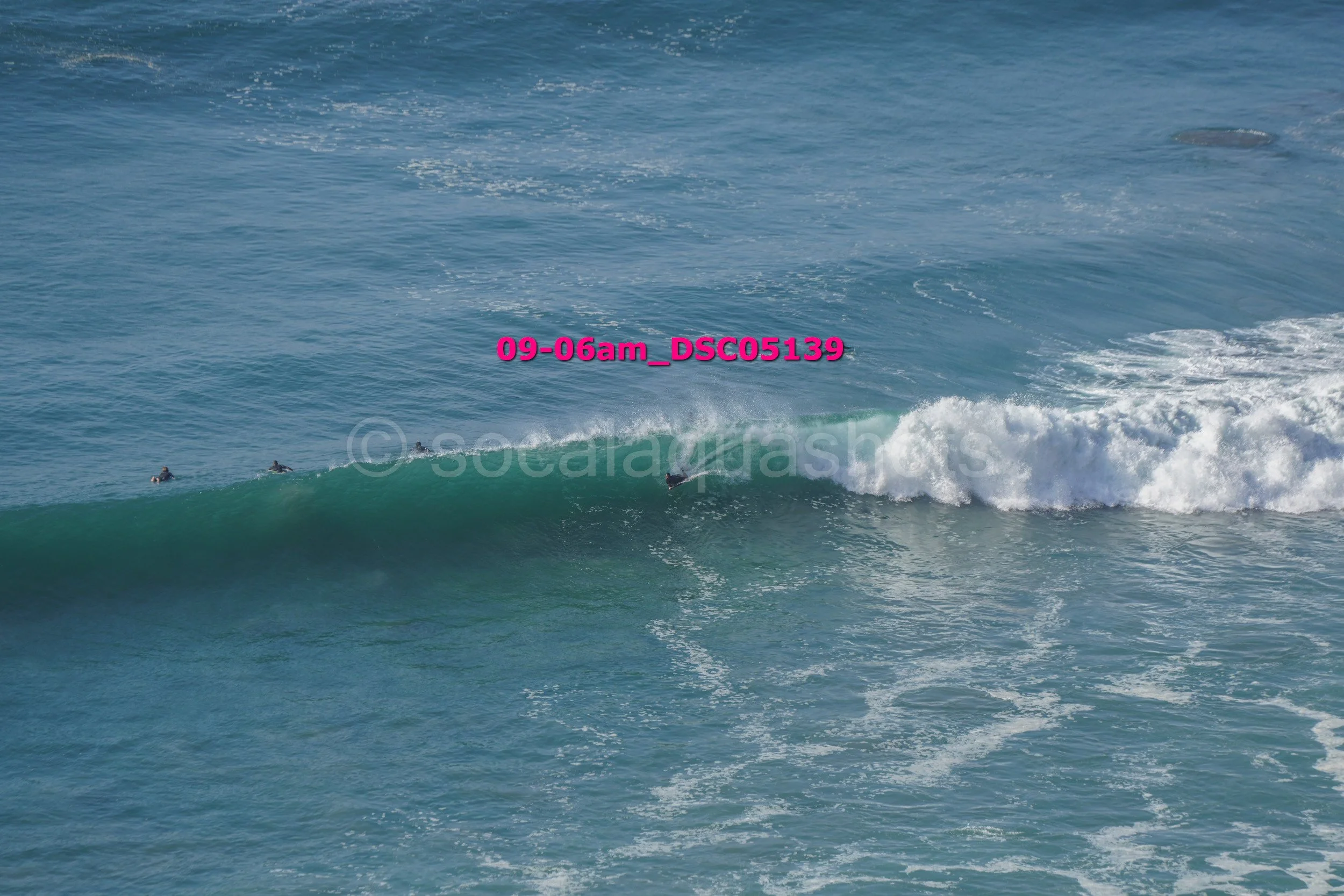 People surfing in the ocean on a large wave with the text '09-06am_DSC05139' in pink across the middle.