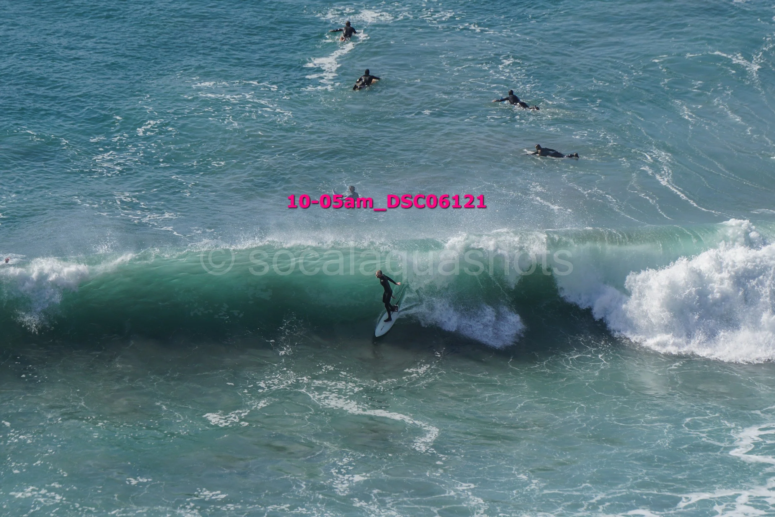 A person surfing on a wave with several other surfers in the water nearby.