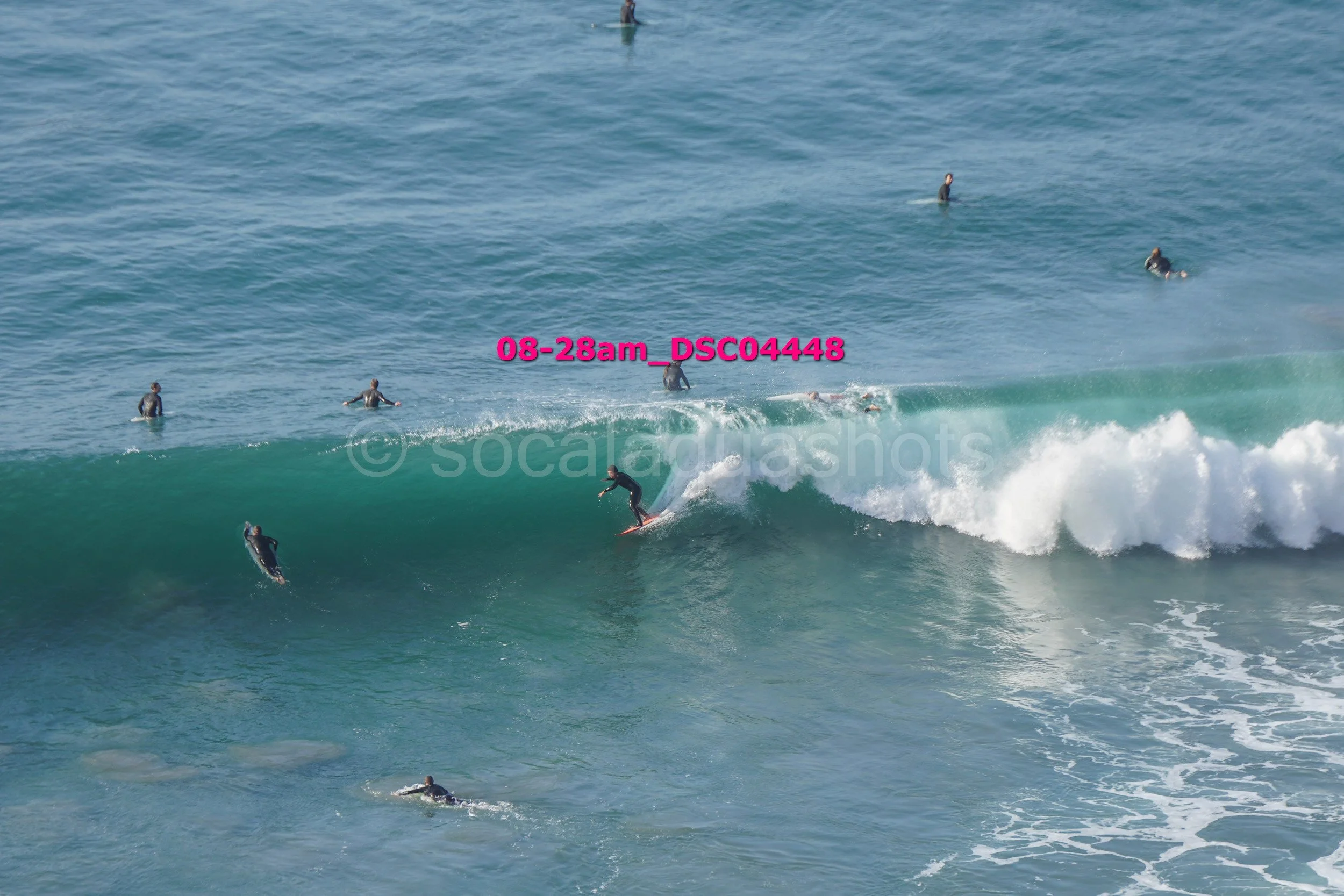 A person surfing on a large wave with several other surfers in the water nearby in the ocean.