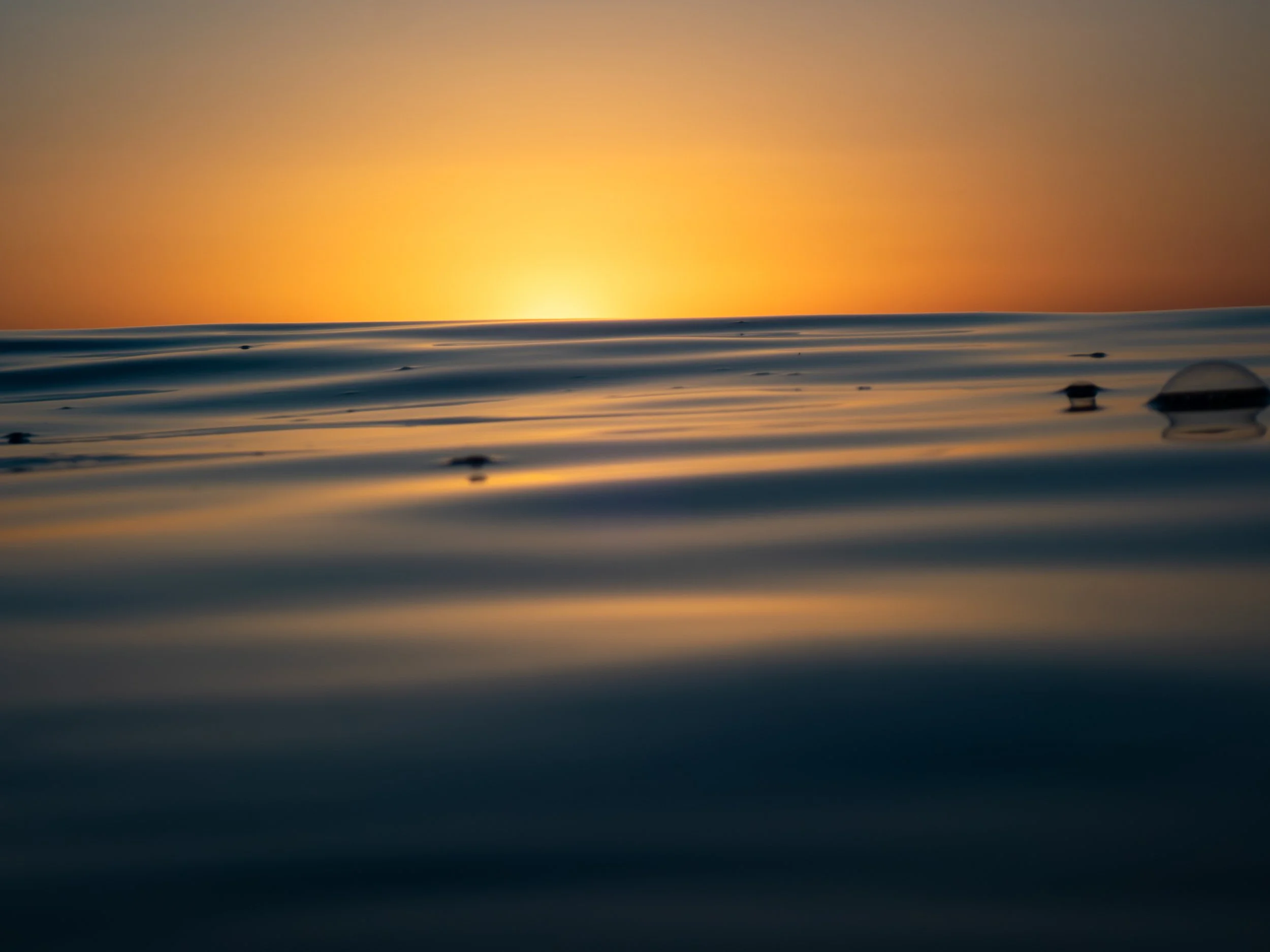 Calm ocean water with reflections of a sunset in the background.