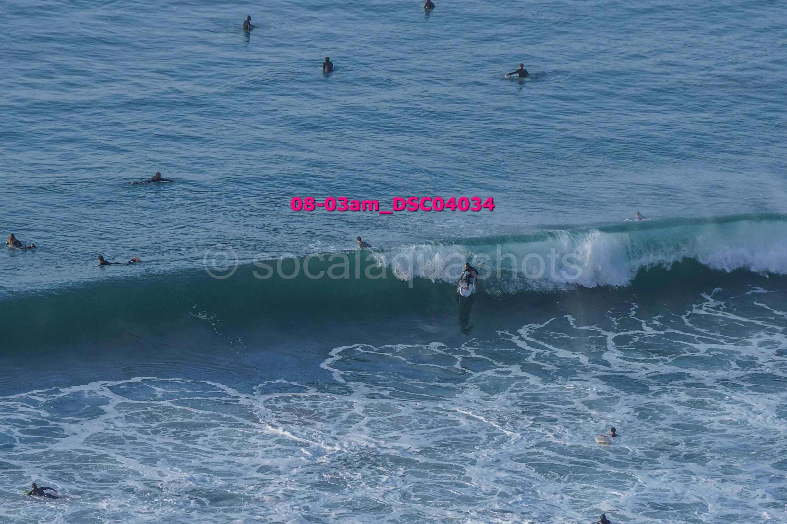Surfer riding a wave with several people in the water watching from afar.