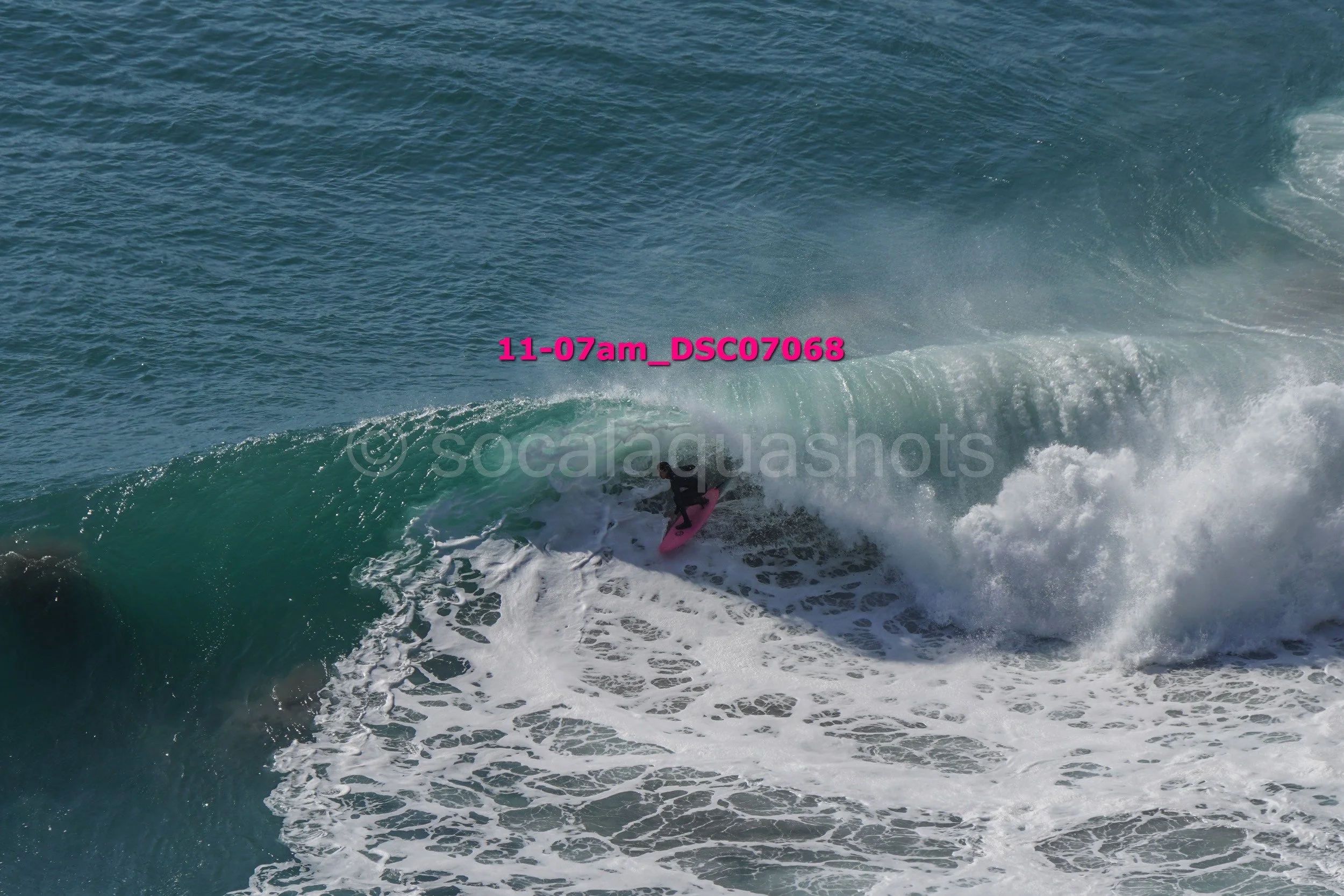 A person surfing on a pink surfboard riding a wave in the ocean.