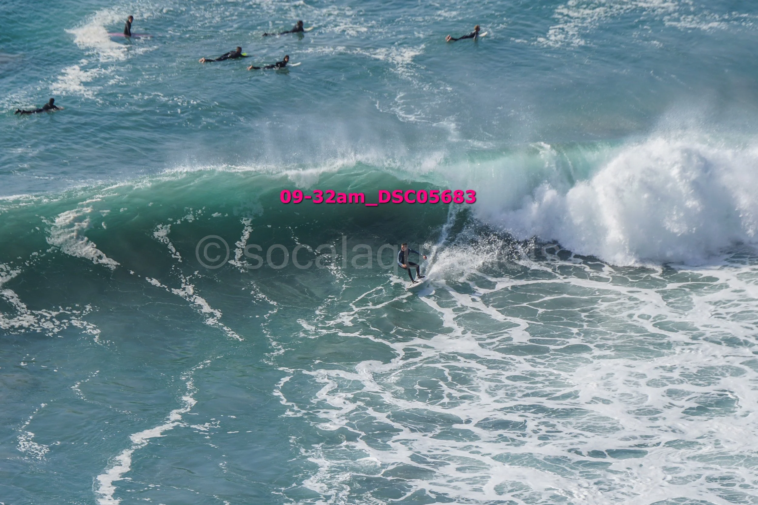 Surfer riding a wave with a group of surfers watching from the water in the background.