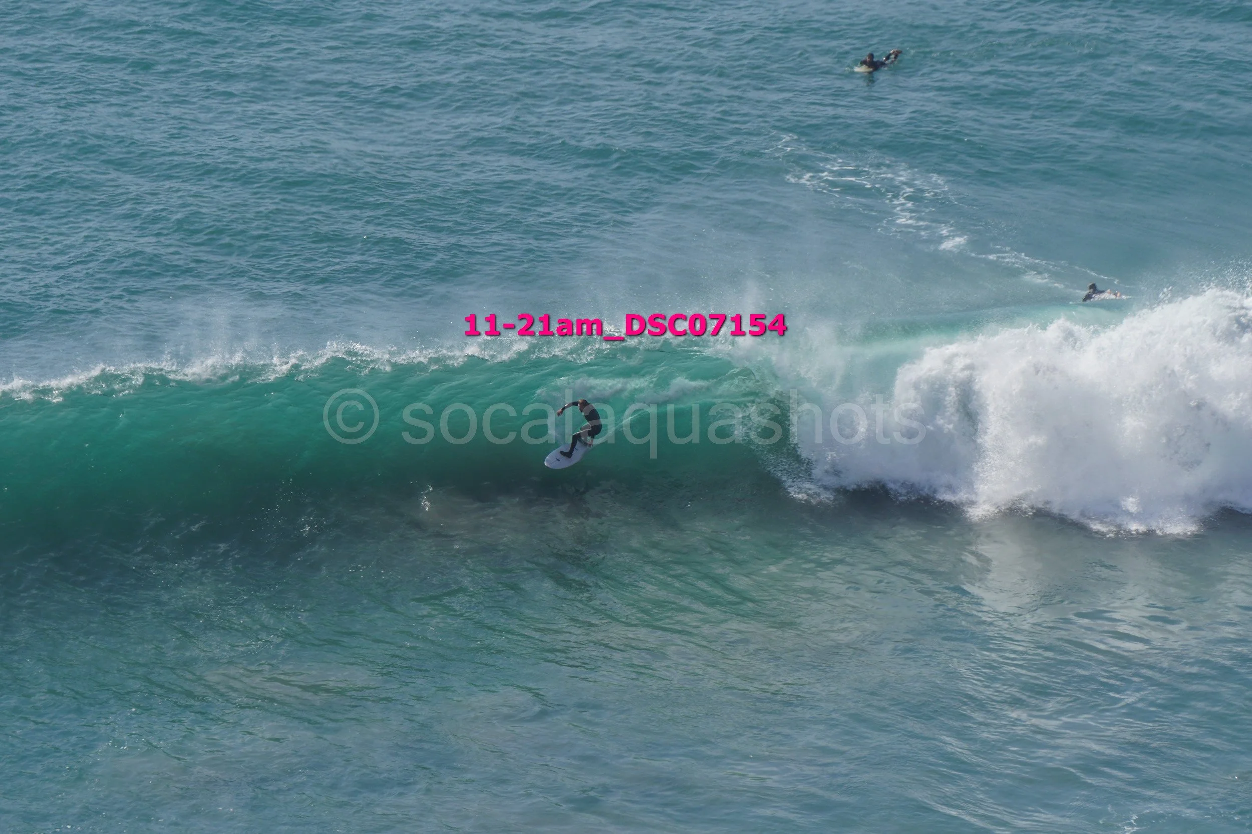 Surfer riding a large wave in the ocean, with two other surfers visible in the background.