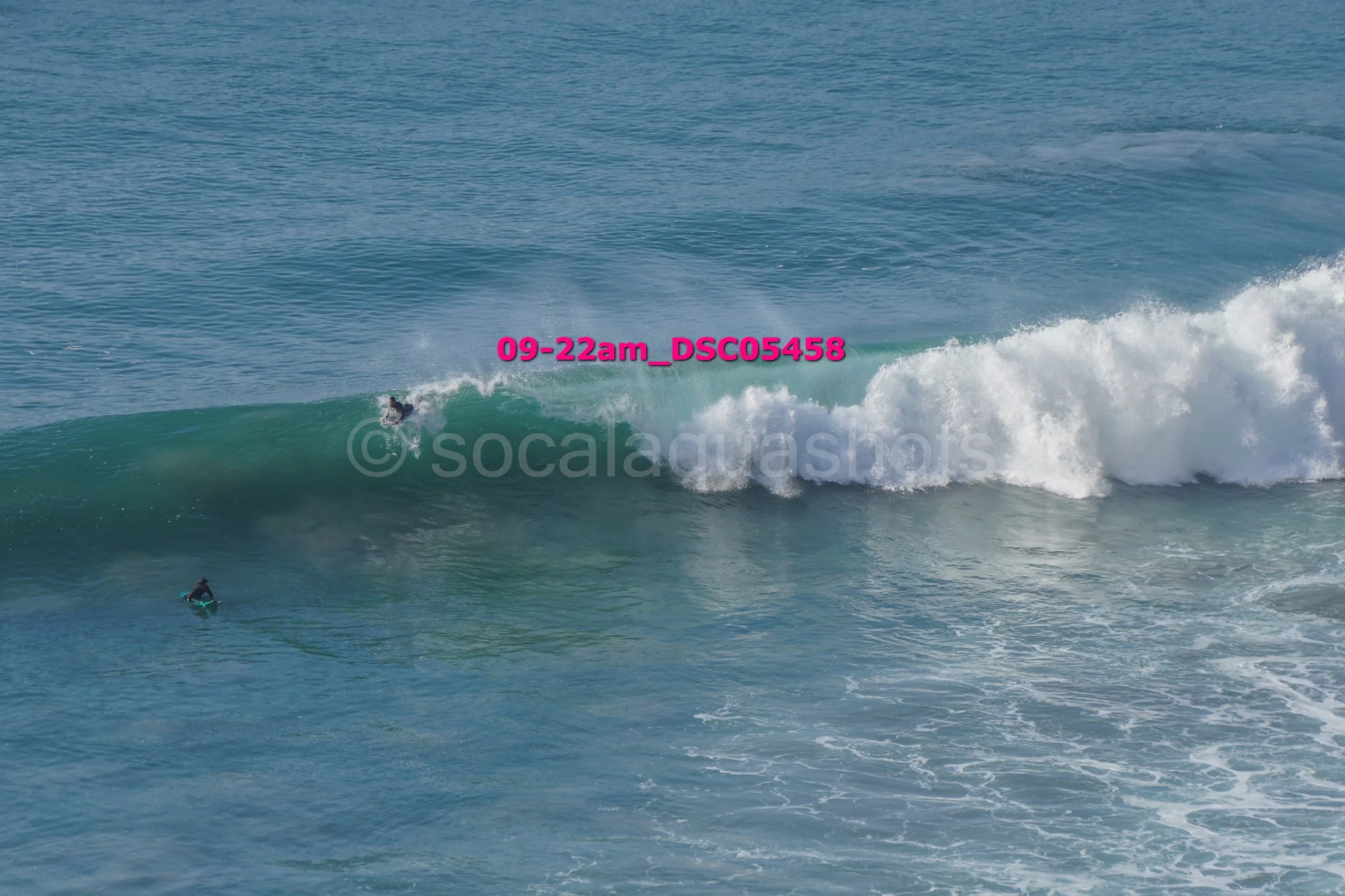 A surfer riding a wave in the ocean, with another person on a surfboard in the water nearby.