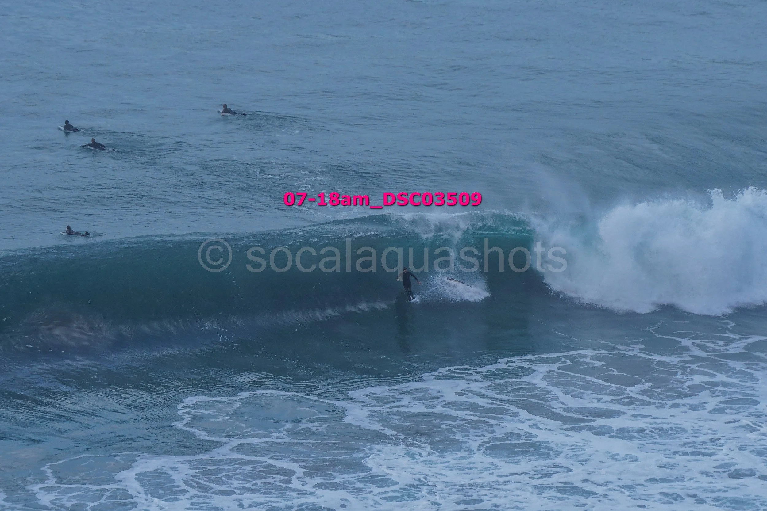 A person surfing on a wave in the ocean, with three other surfers in the distance.