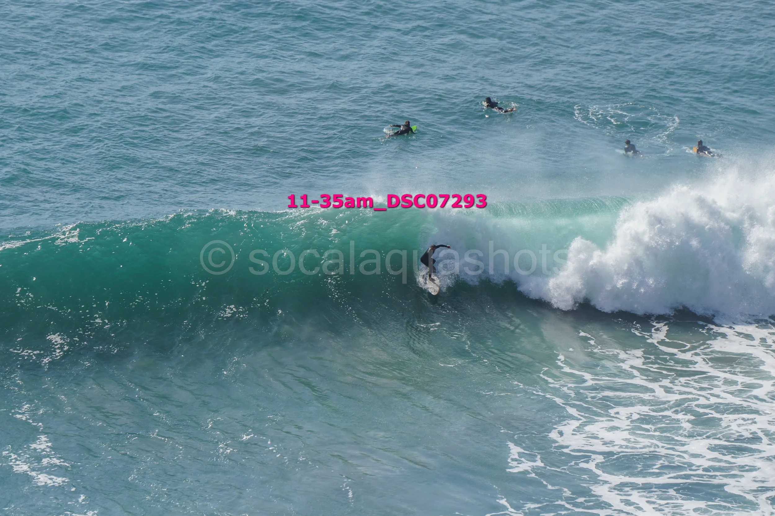 Surfer riding a wave with a group of people swimming in the water nearby.