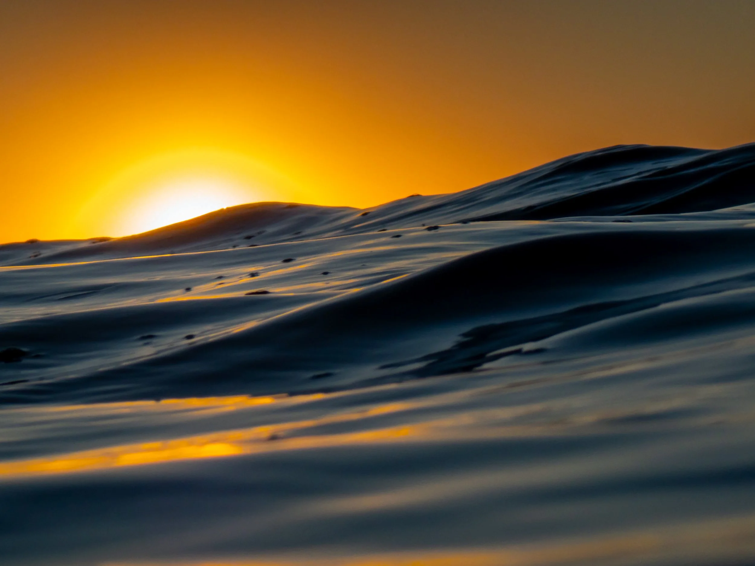 Sunset over ocean waves with the sun near the horizon, casting a warm glow and reflecting off the water's surface.