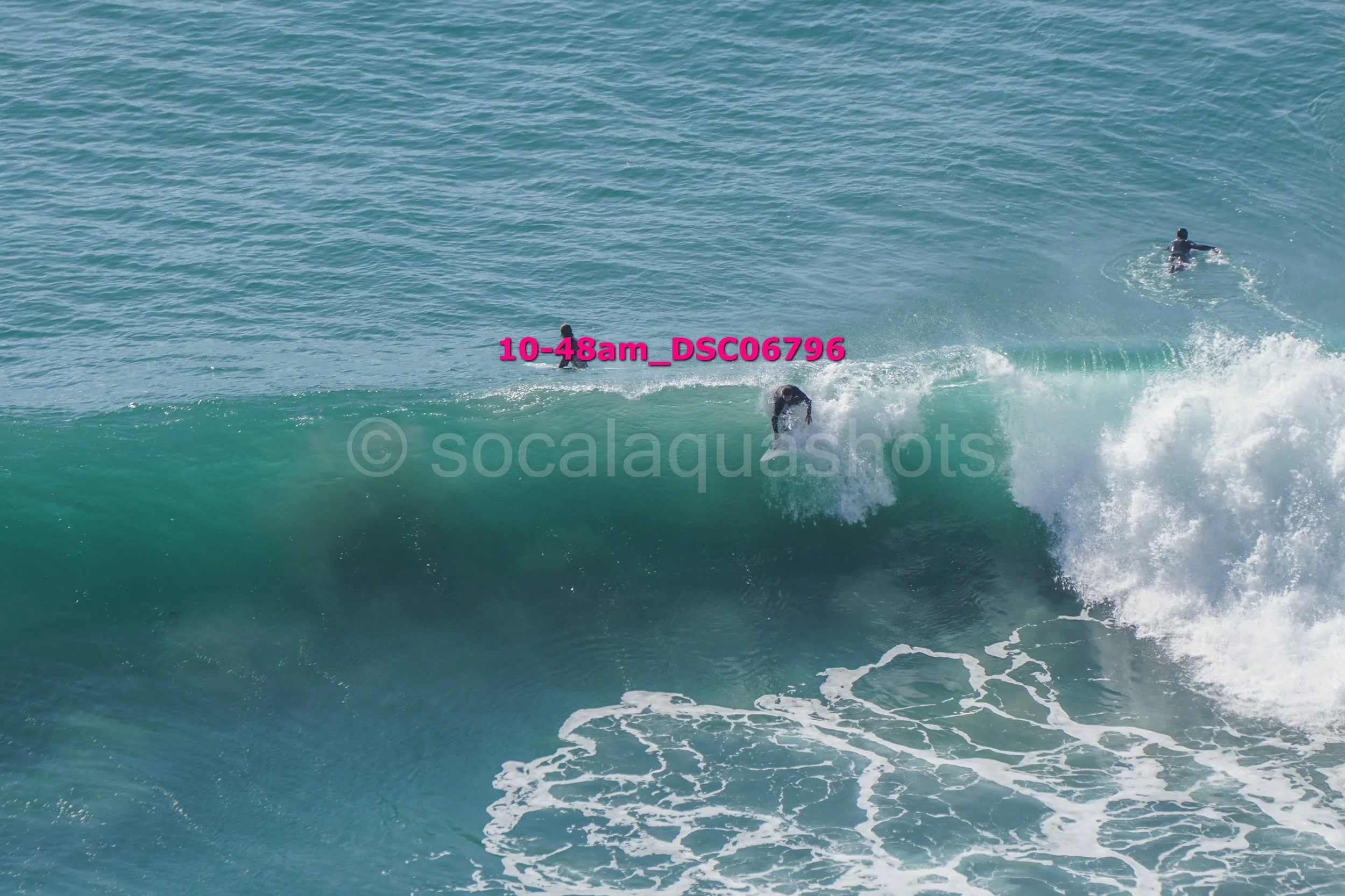 A person surfing a wave with two other people swimming in the background in the ocean.