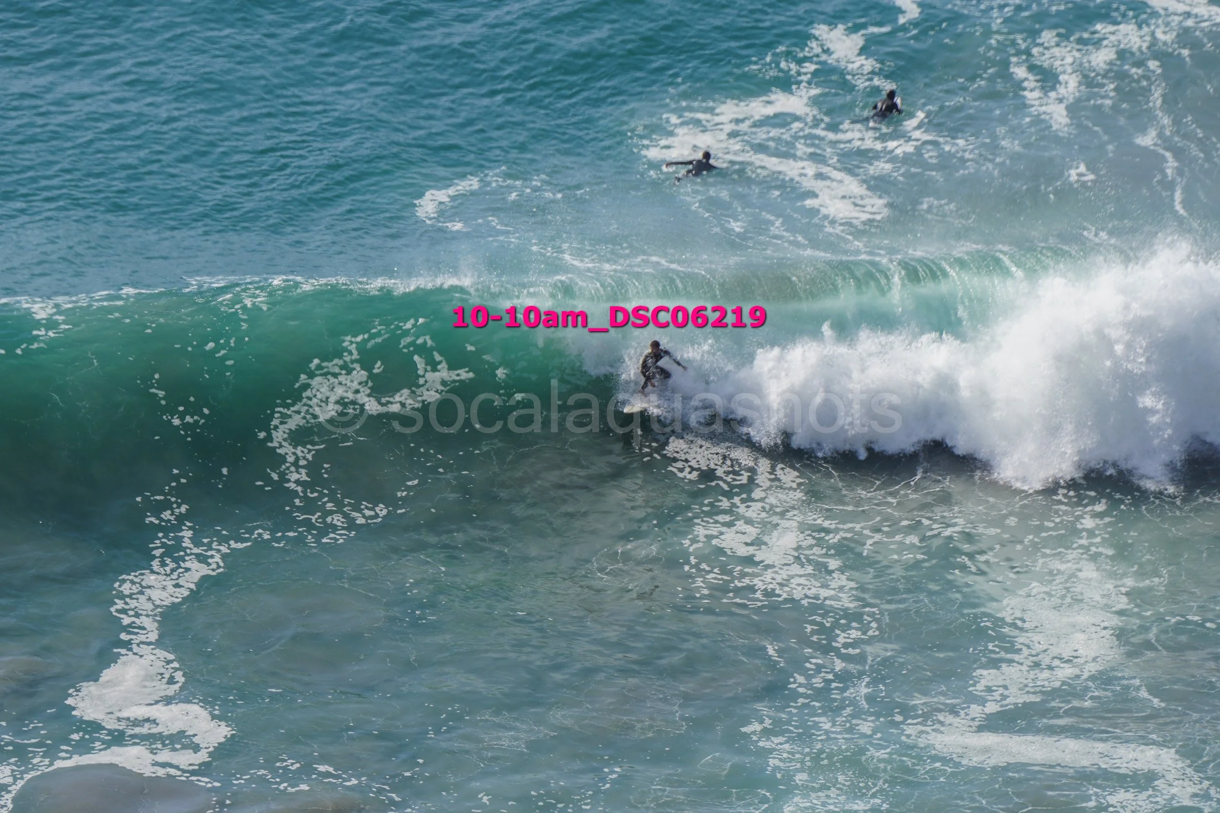 Surfer riding a wave in the ocean, with other surfers in the background.