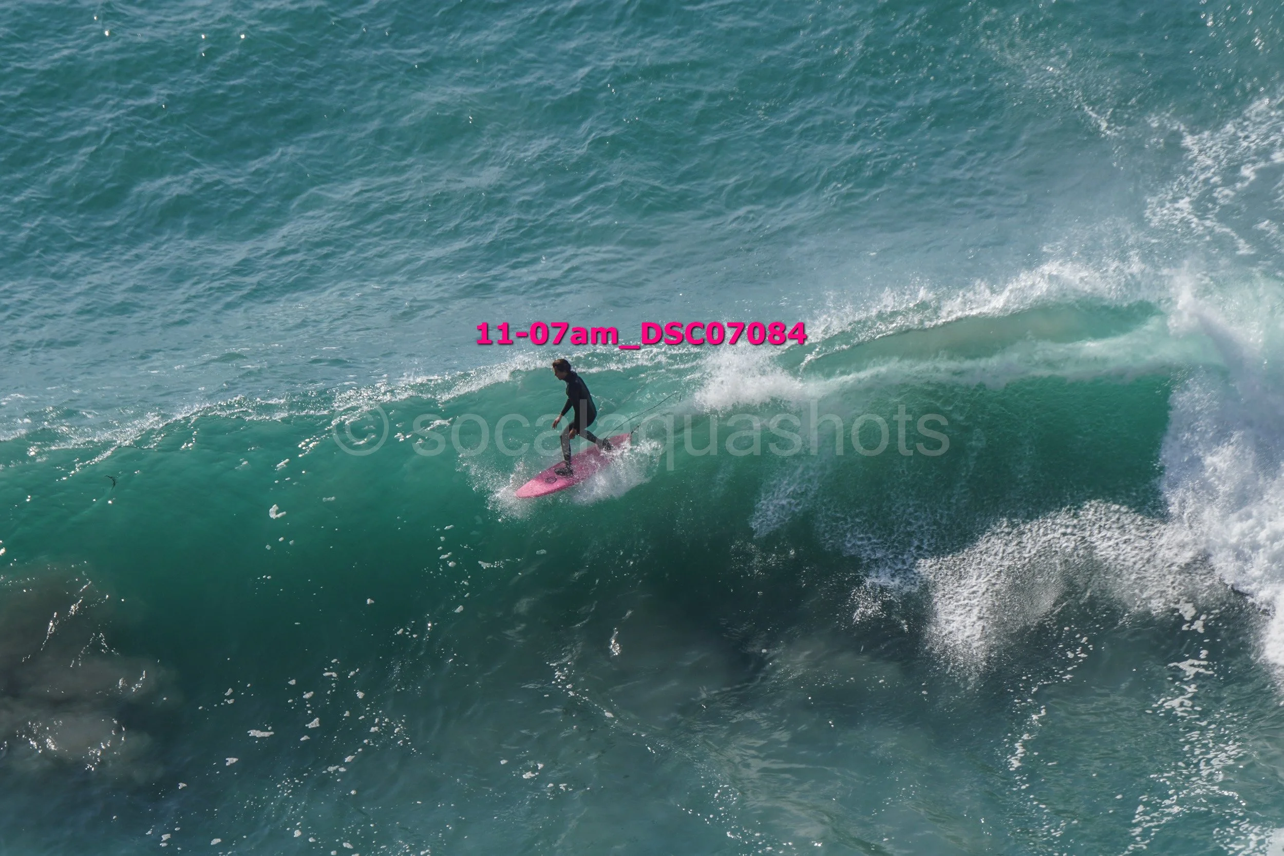 A person surfing on a pink surfboard riding a wave in the ocean