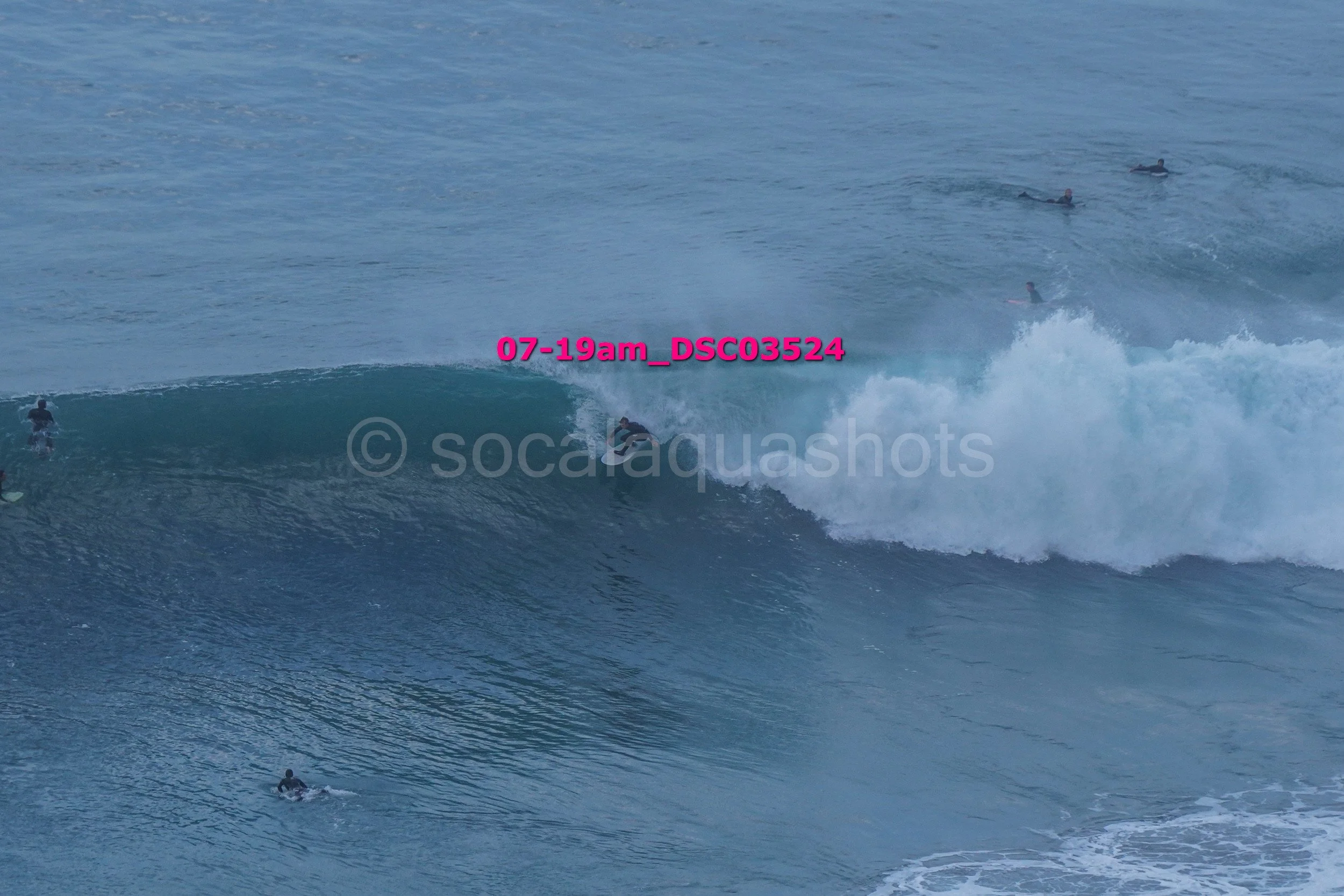 A surfer riding a wave with multiple surfers in the background in the ocean.
