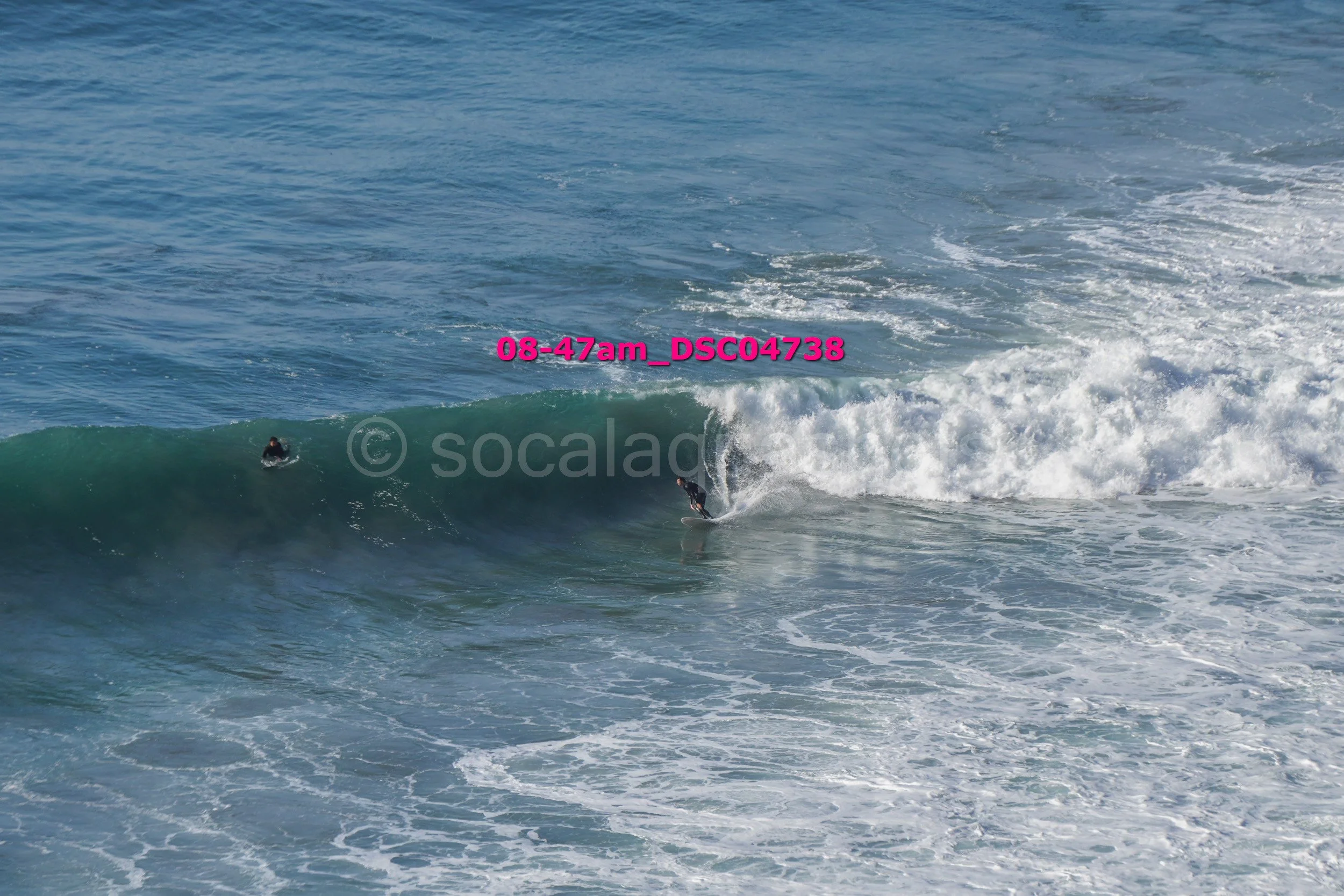 A person surfing on a wave in the ocean, with another person swimming nearby.