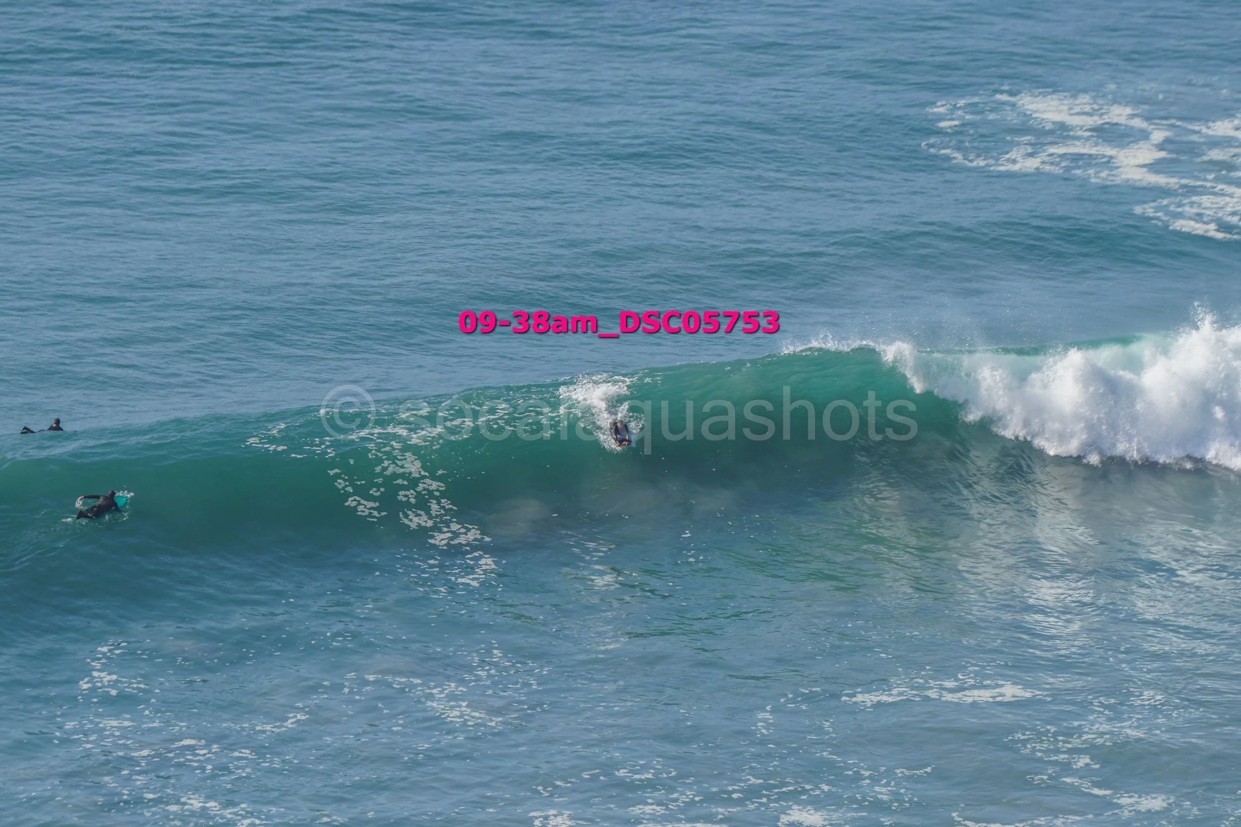 Surfer riding a large wave in the ocean with other surfers nearby.