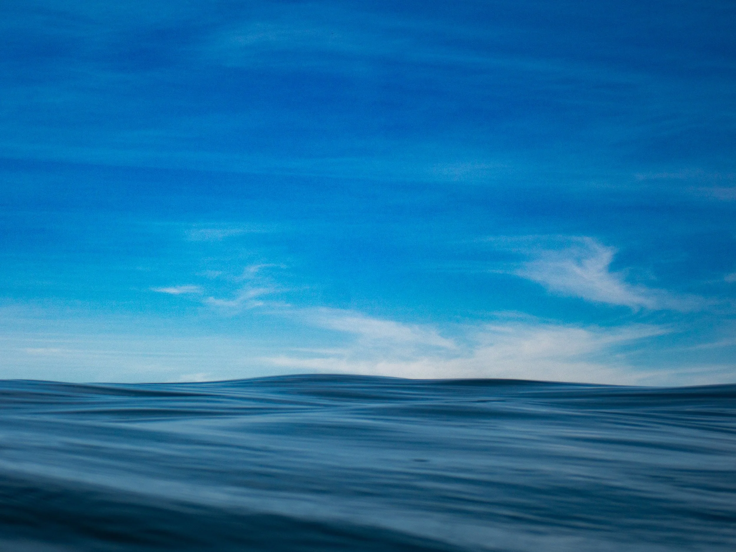 A calm ocean view with blue water and a partly cloudy sky.