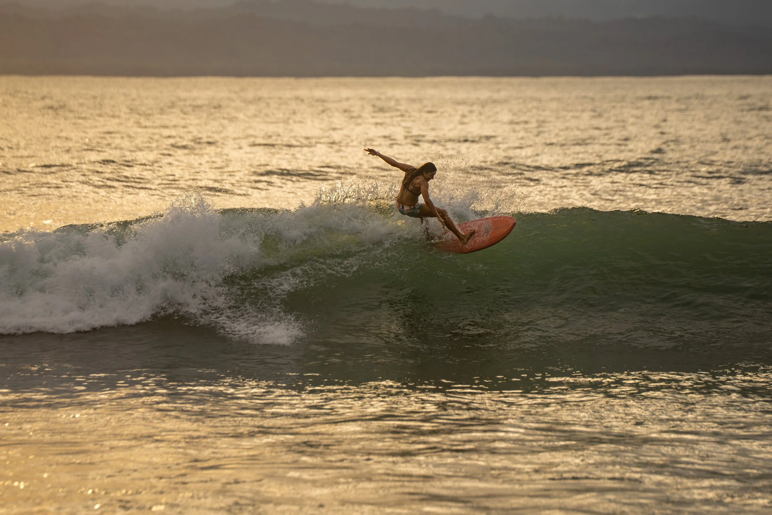 A person riding a surfboard on a wave during sunset at the ocean.
