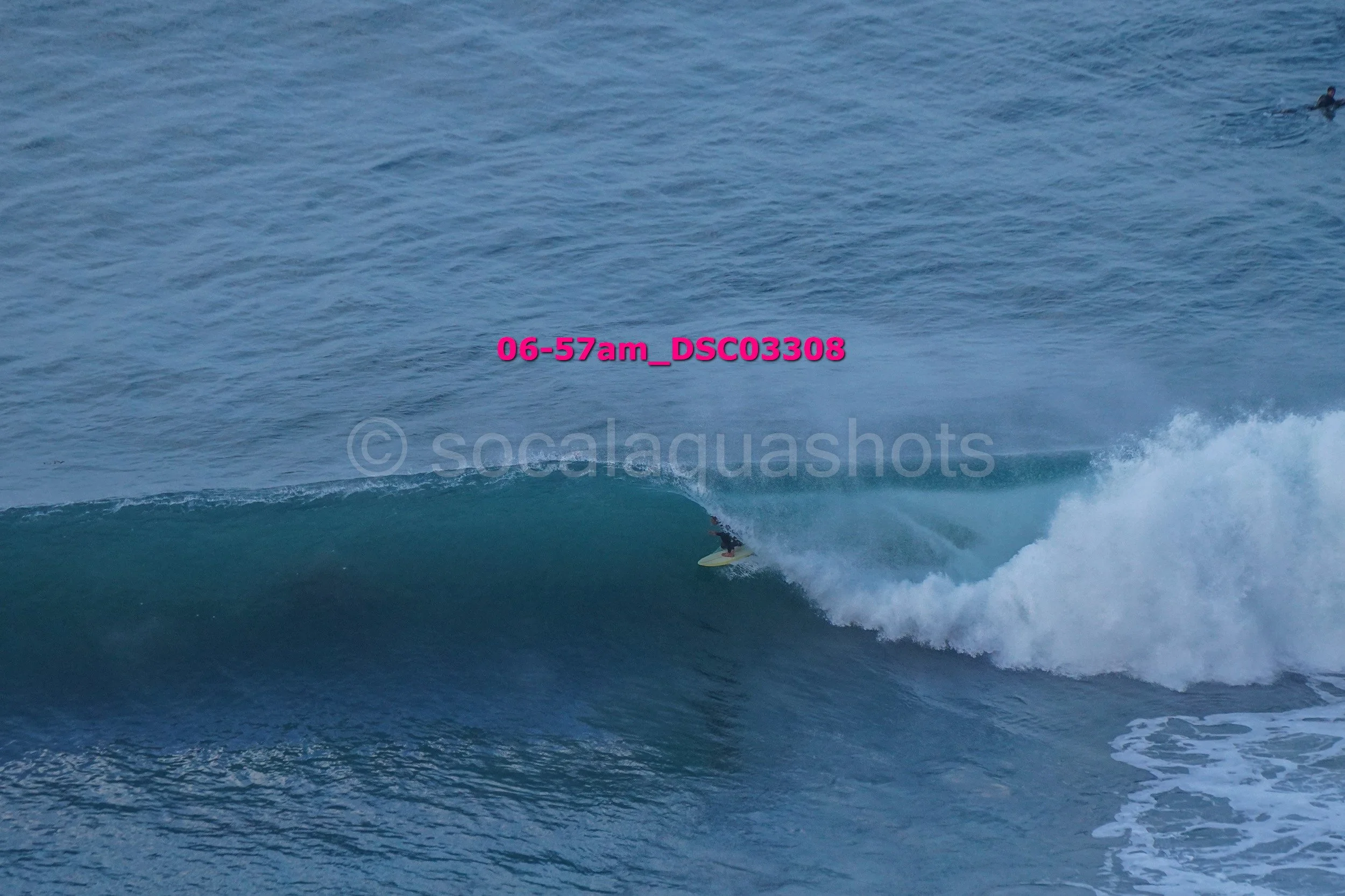 A person surfing a wave in the ocean with the water appearing blue and white foam on the wave's crest.